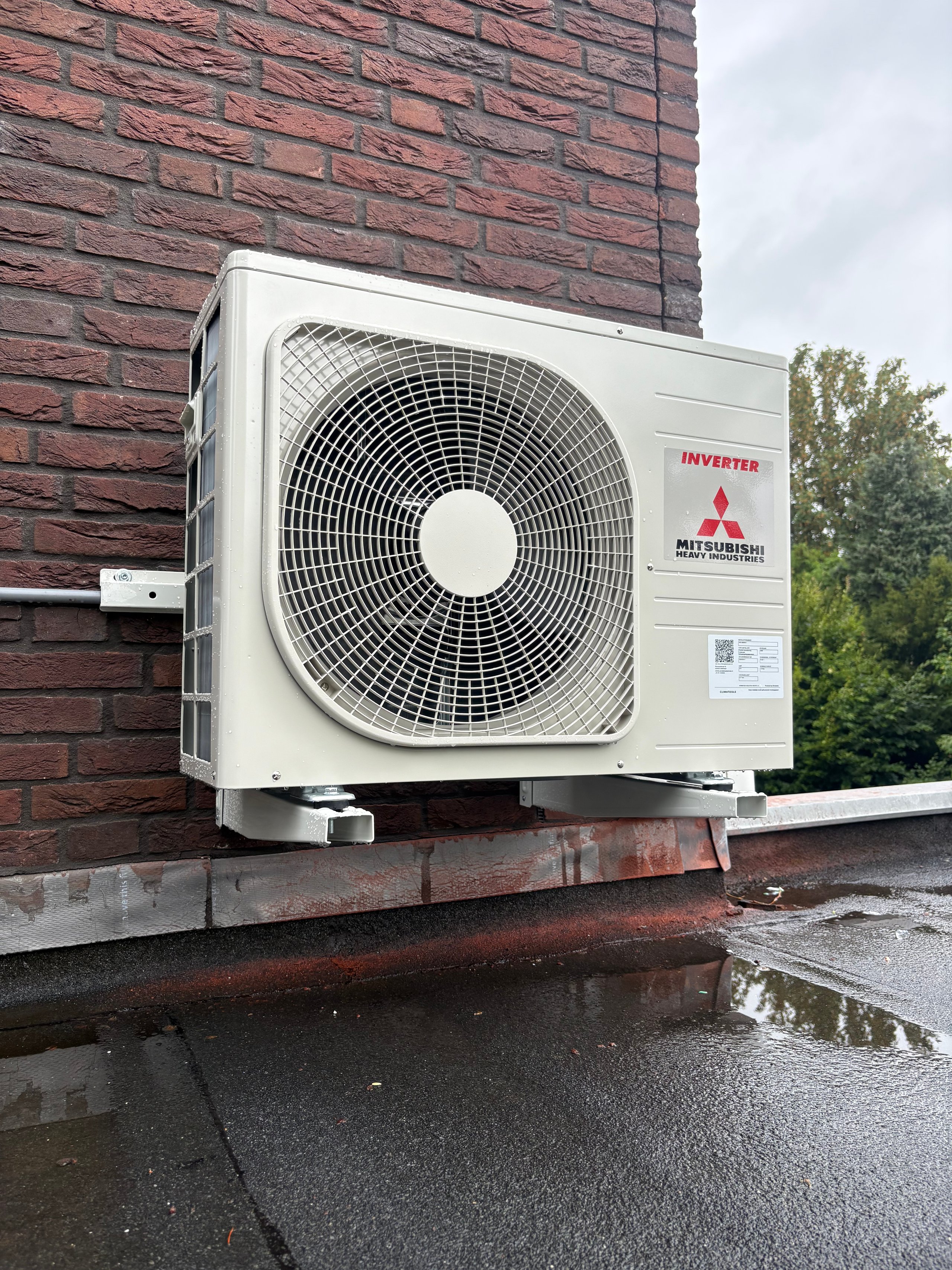 Mitsubishi inverter air conditioning unit mounted on a brick building wall with wet rooftop surface
