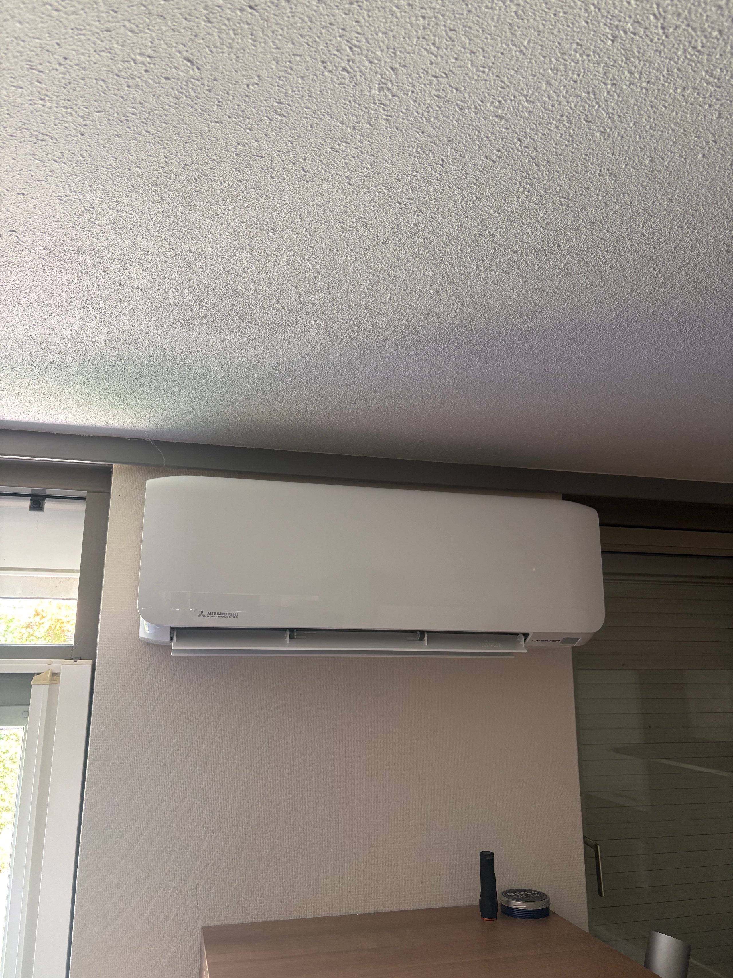White split-type air conditioning unit mounted on a beige wall above a desk near a window