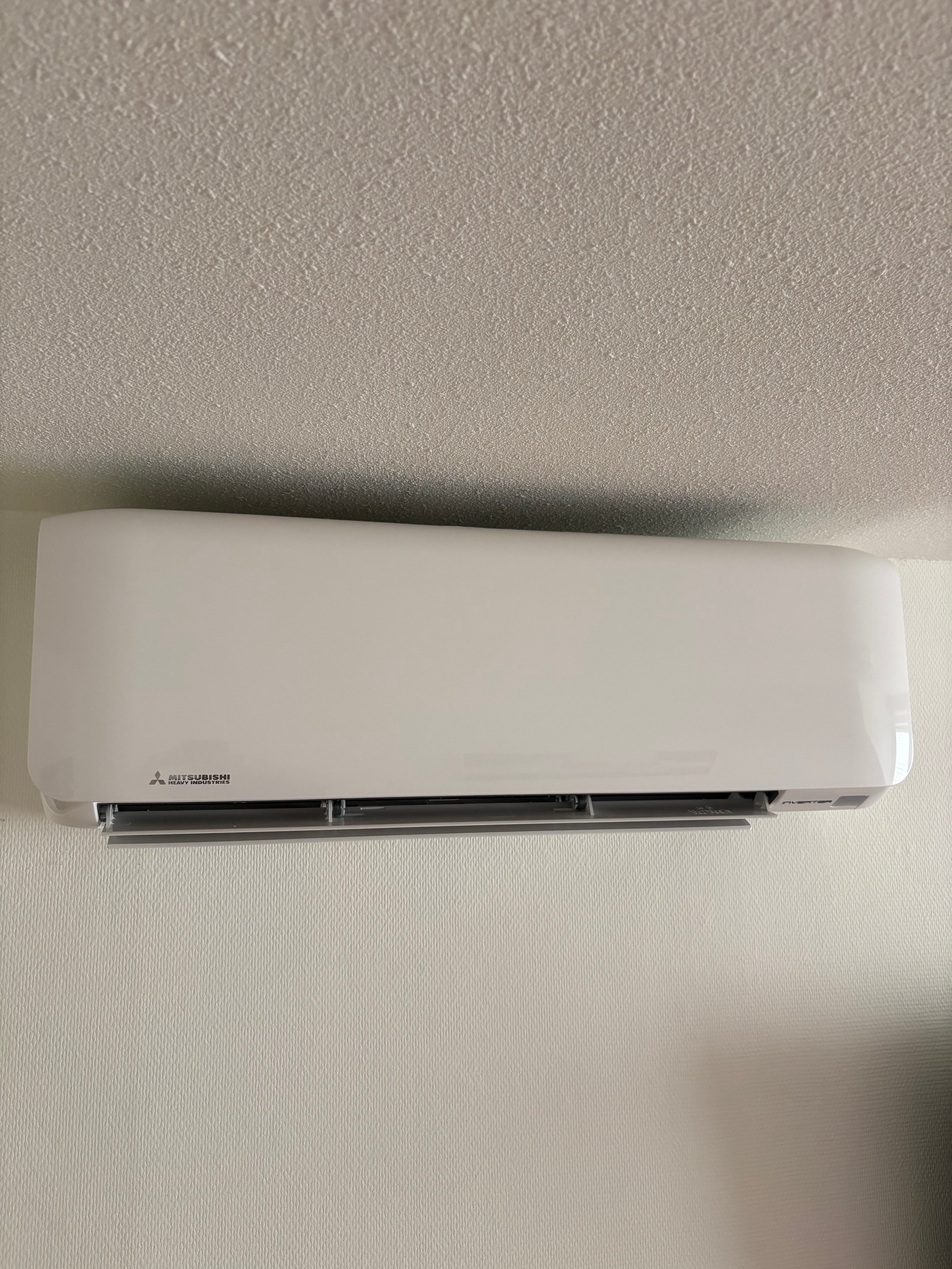 White Mitsubishi ductless mini-split air conditioner unit mounted on a beige textured wall
