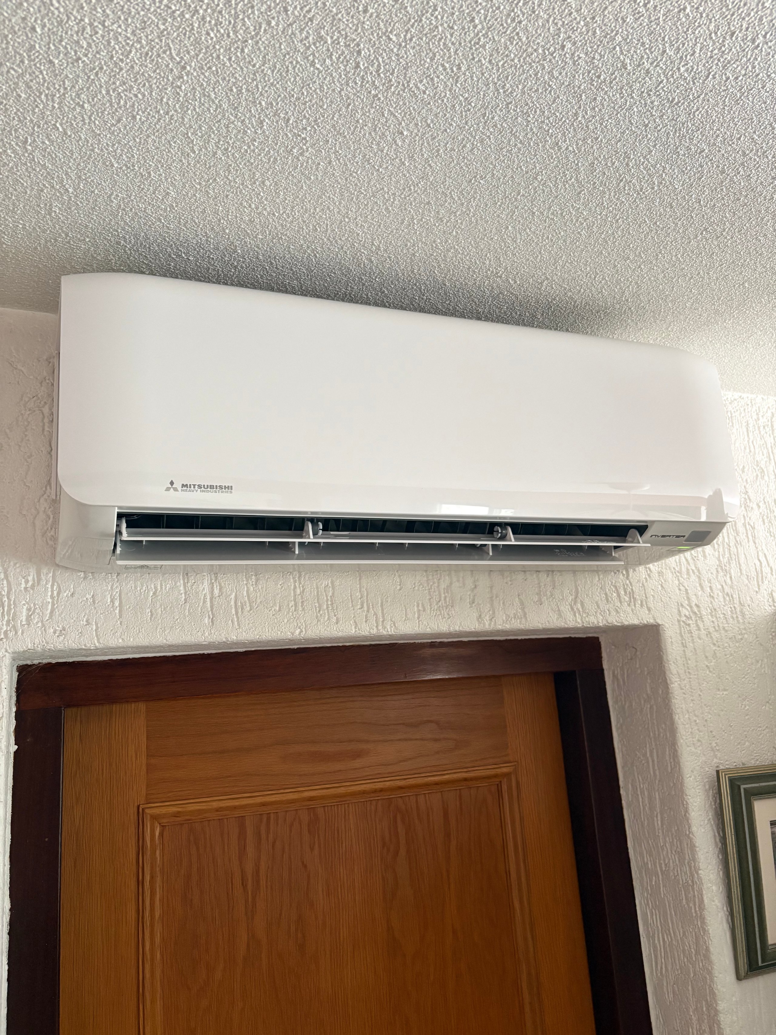 White Mitsubishi split air conditioning unit mounted on wall above a wooden door
