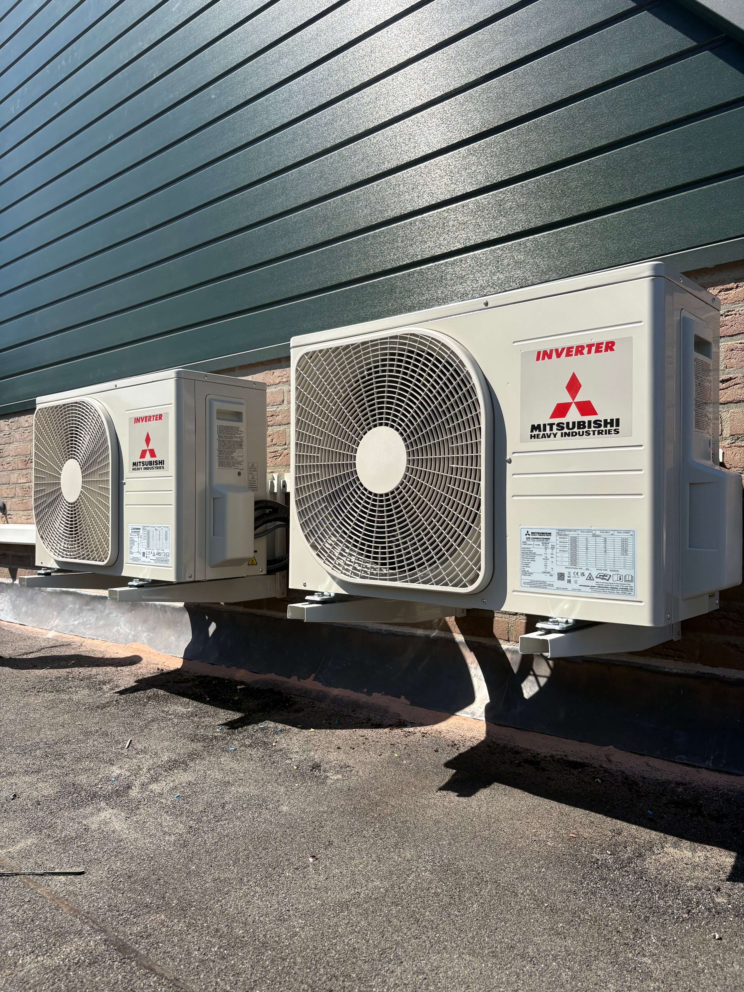 Mitsubishi inverter heat pump units mounted on the exterior wall of a building with blue corrugated siding