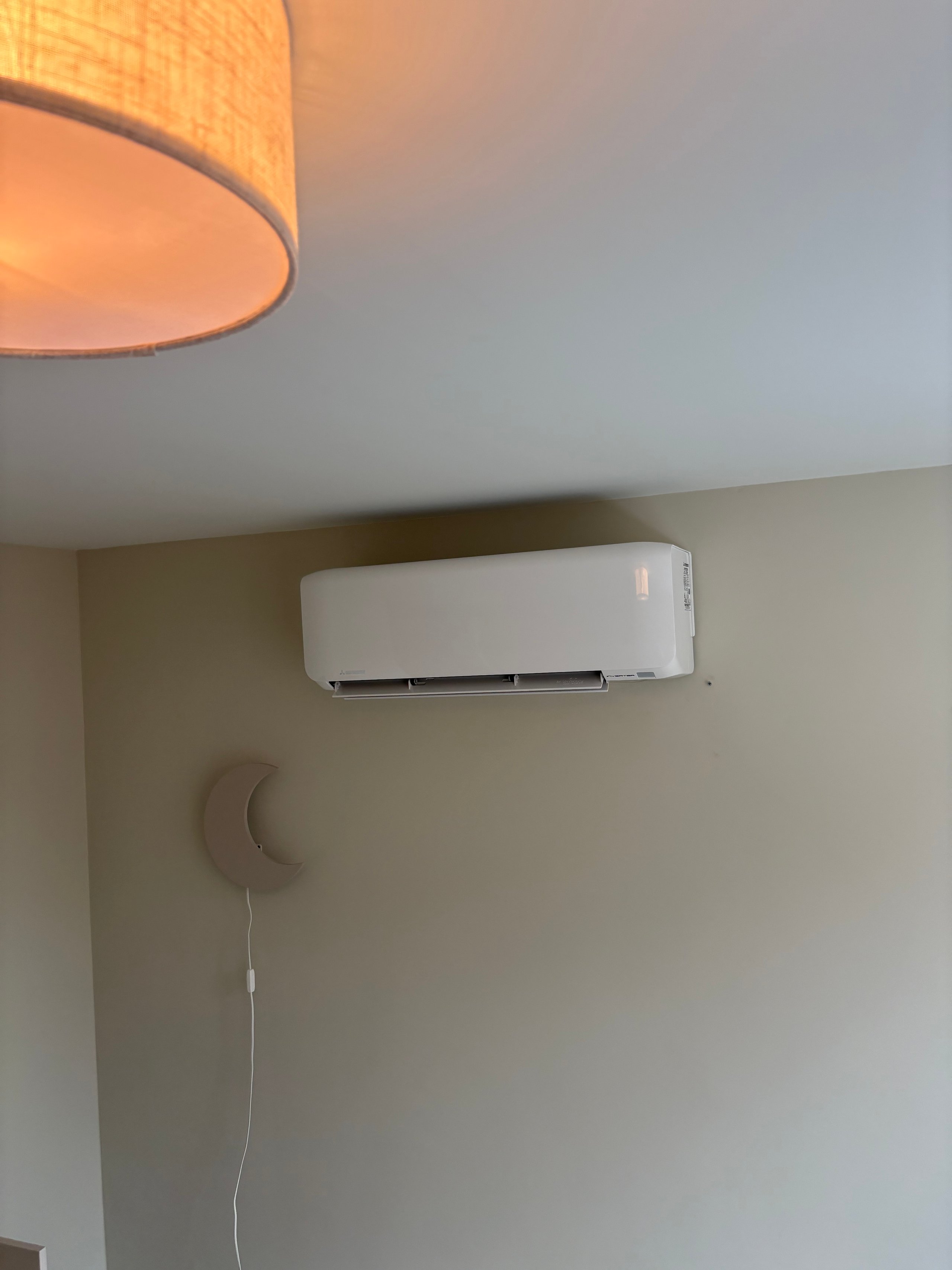 Interior ceiling with white split air conditioning unit mounted on beige wall and cylindrical fabric pendant light fixture