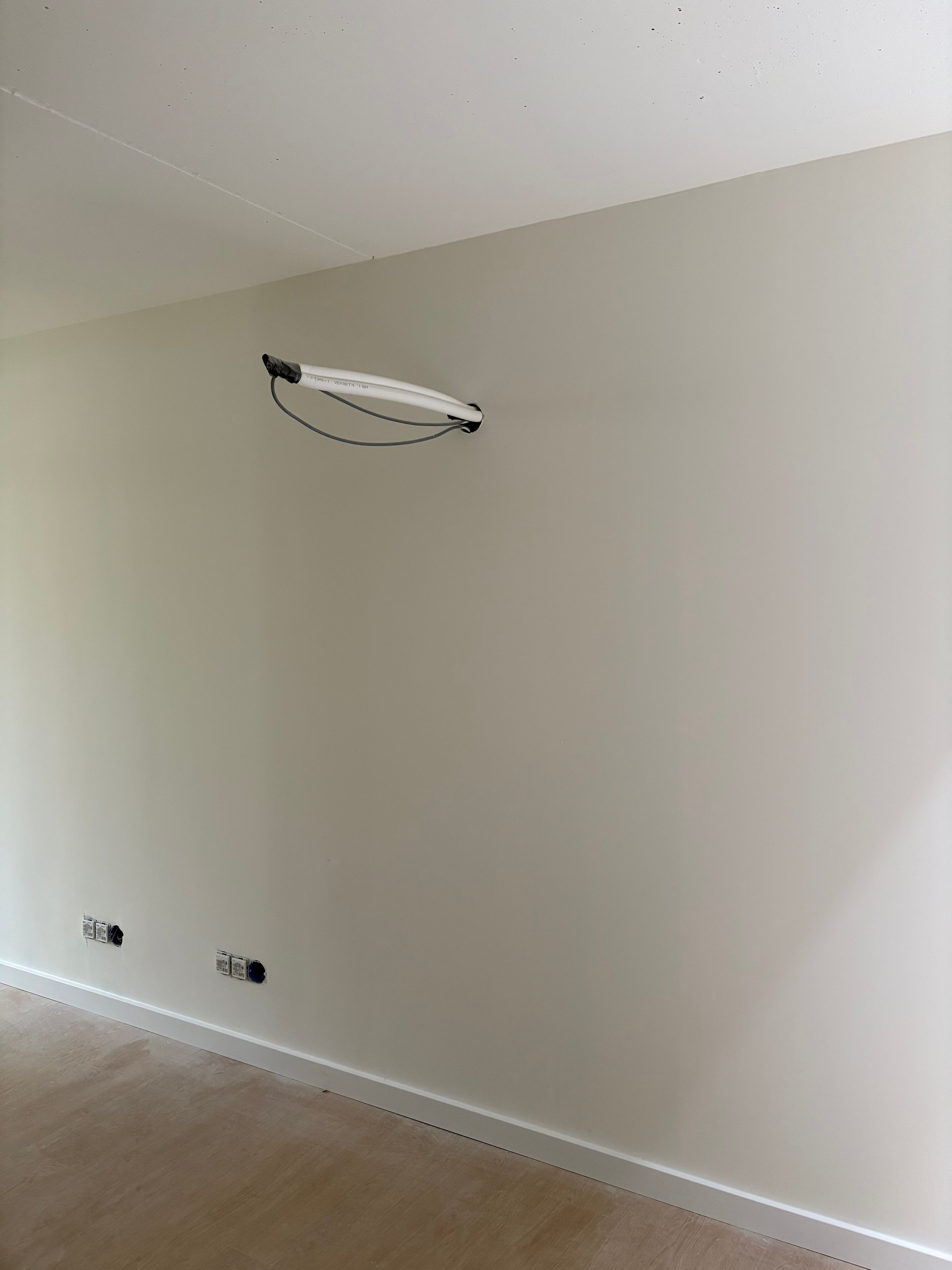 Empty room with beige walls, wooden floor, two electrical outlets, and a single ceiling-mounted light fixture