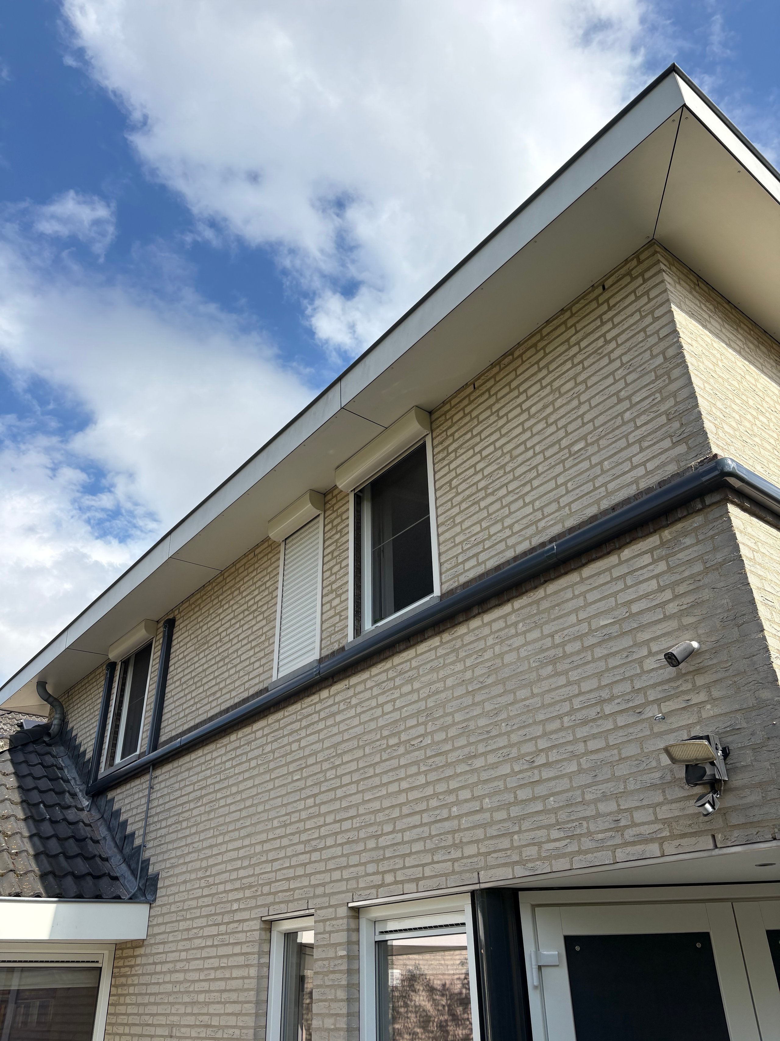 Modern two-story cream brick house with large upper windows against blue sky with white clouds