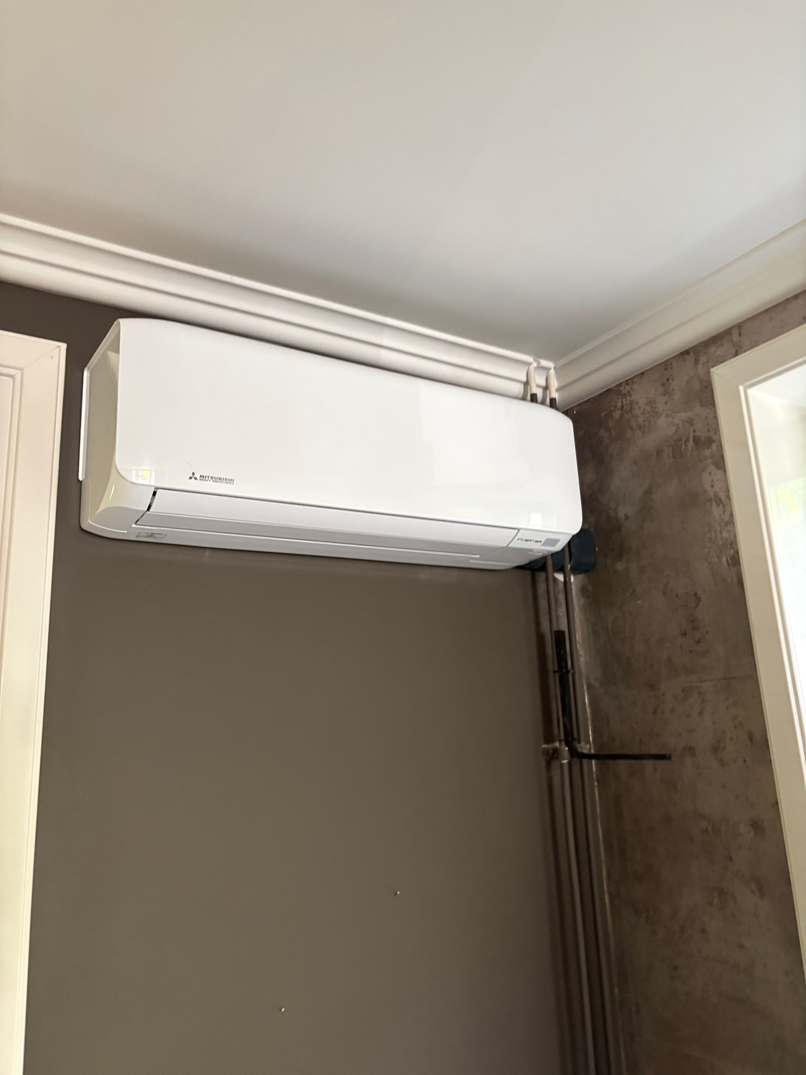 White wall-mounted air conditioning unit installed on a beige wall with dark accent wall in a modern interior space