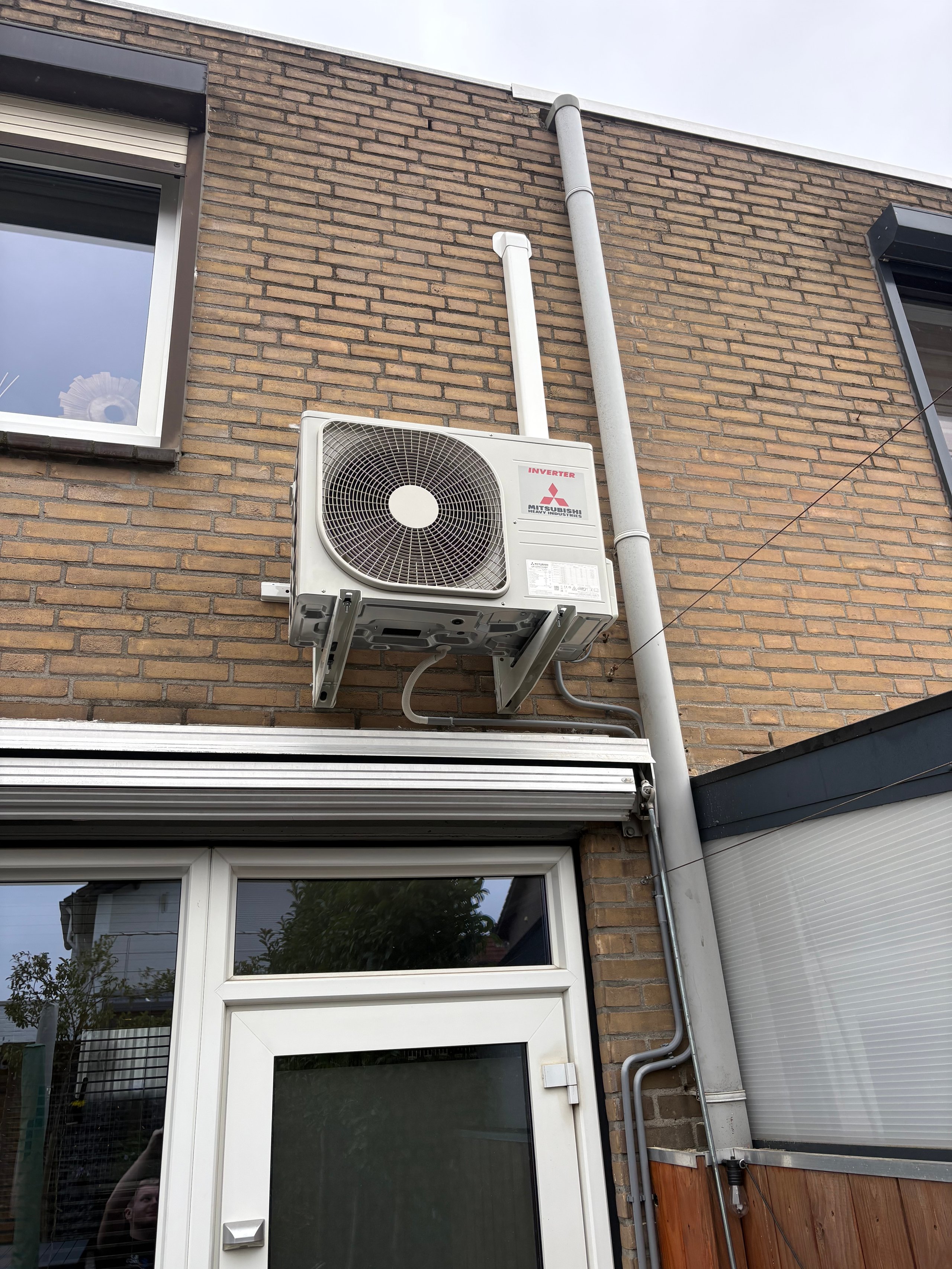 Mitsubishi air conditioning unit mounted on brick exterior wall above white door