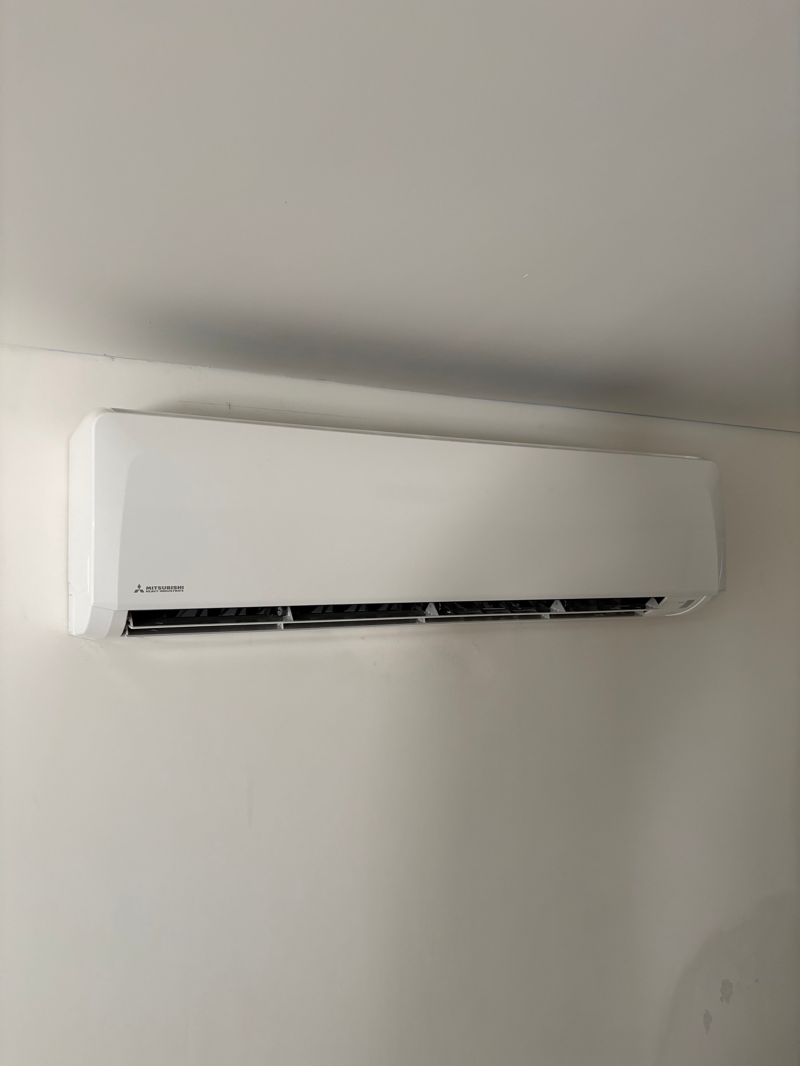 White Mitsubishi air conditioning unit mounted on a wall with black vents