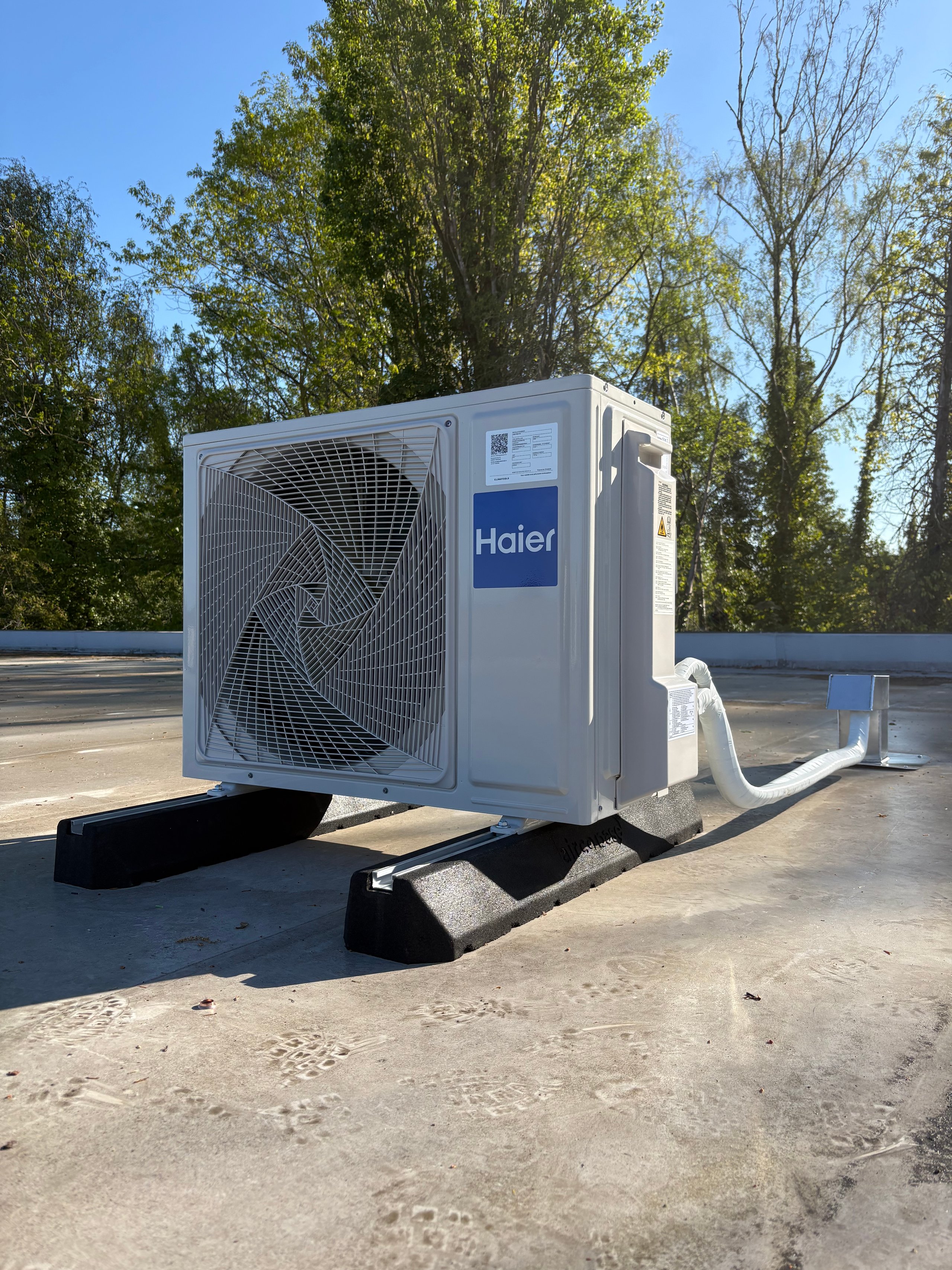Haier air conditioning outdoor unit mounted on a concrete rooftop with trees in the background
