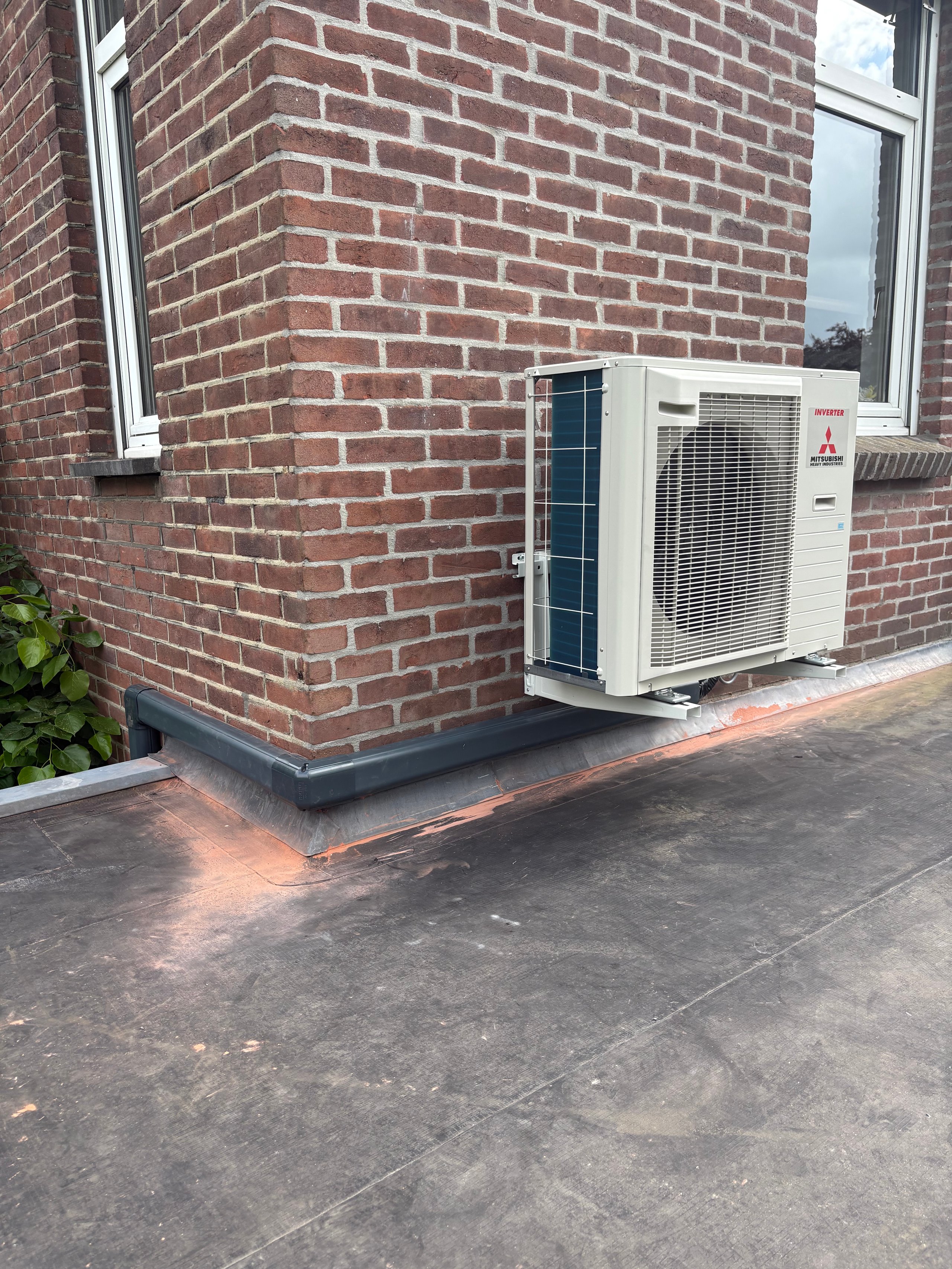 Outdoor heat pump unit mounted on concrete pad against brick wall with windows