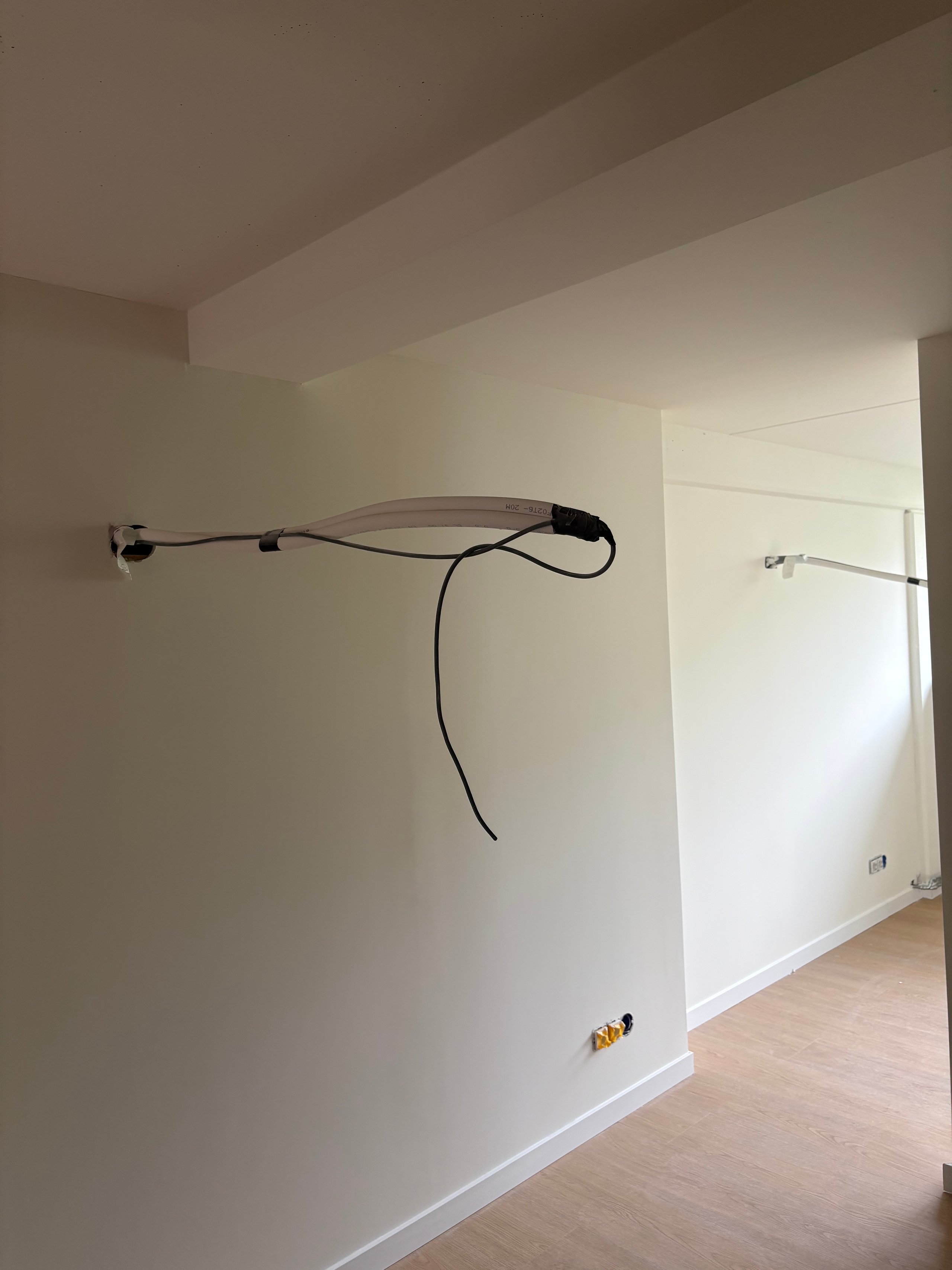 Interior room with white walls, wooden floor, and a black cable or cord draped across mounted brackets on the wall