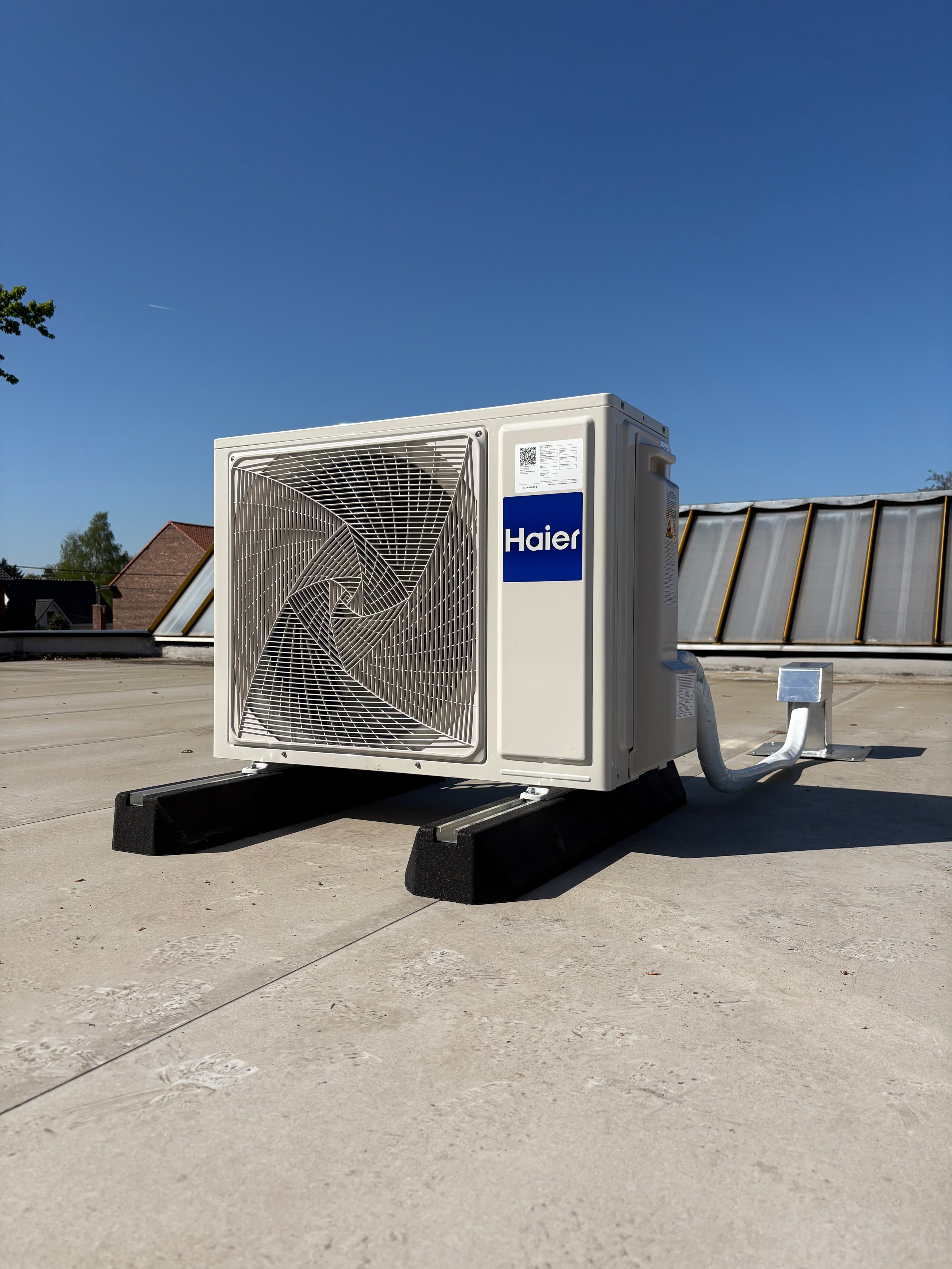 Haier heat pump unit mounted on a concrete rooftop with clear blue sky and industrial surroundings
