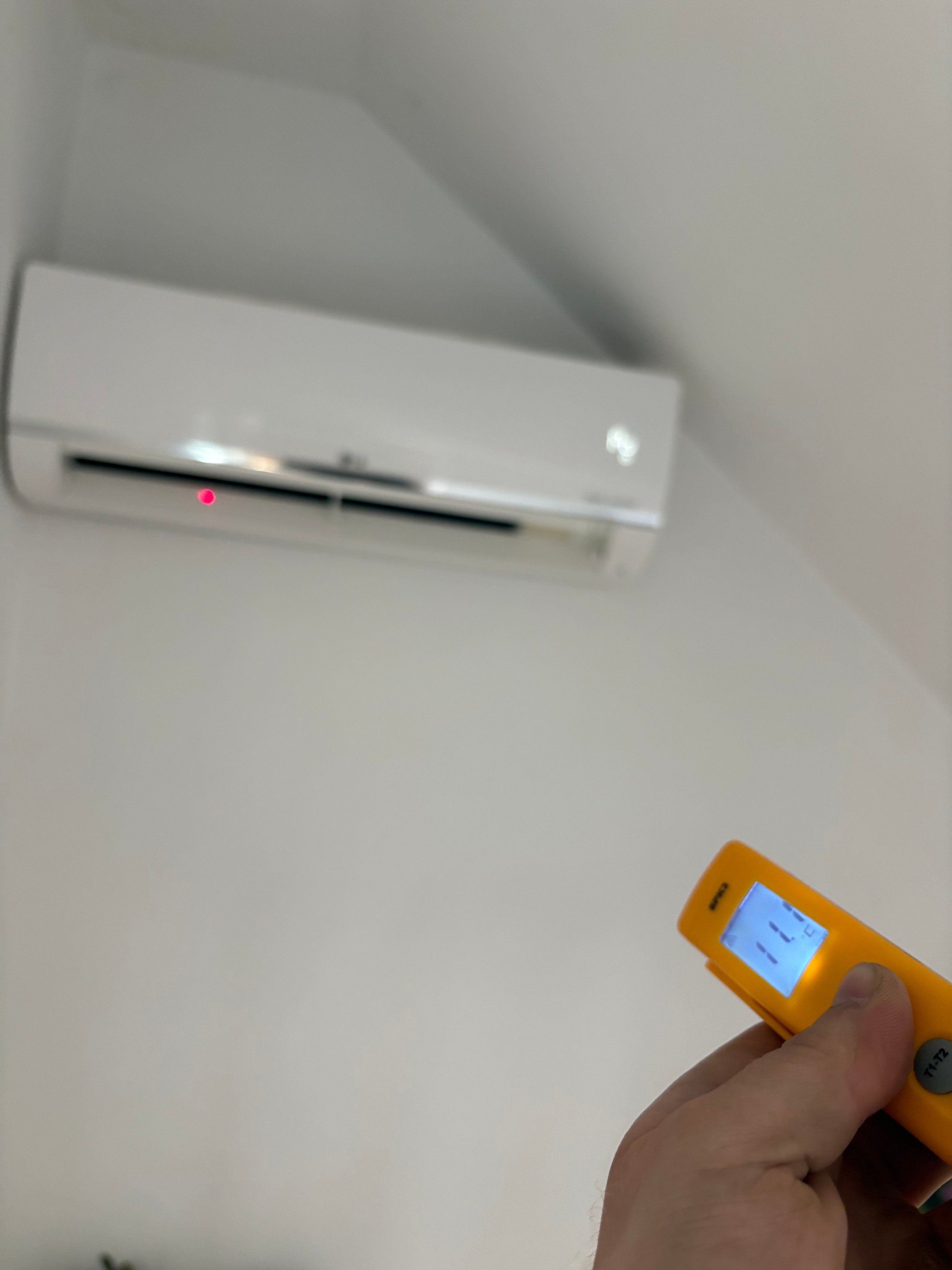Hand holding yellow thermometer measuring temperature of white wall-mounted air conditioning unit