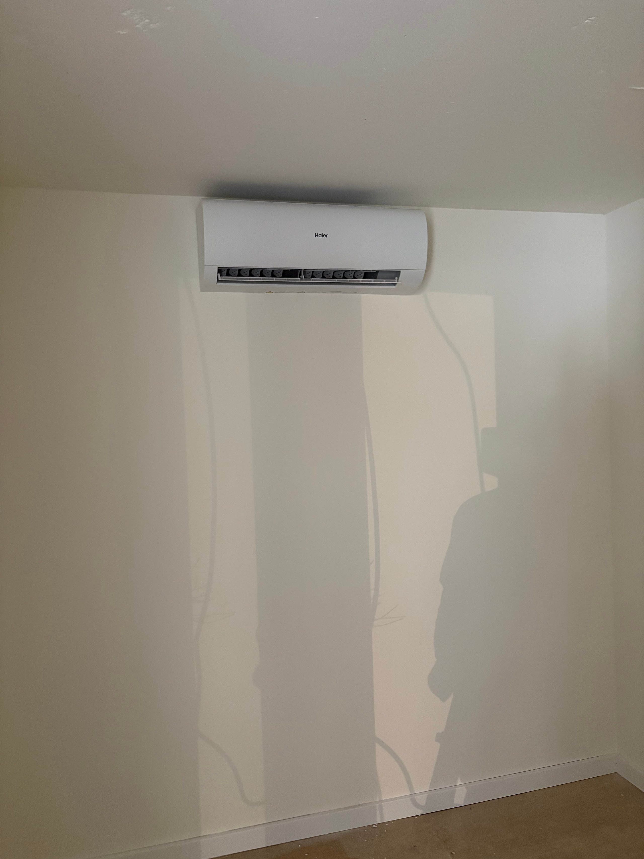 White wall-mounted air conditioning unit installed on a beige wall in an empty room