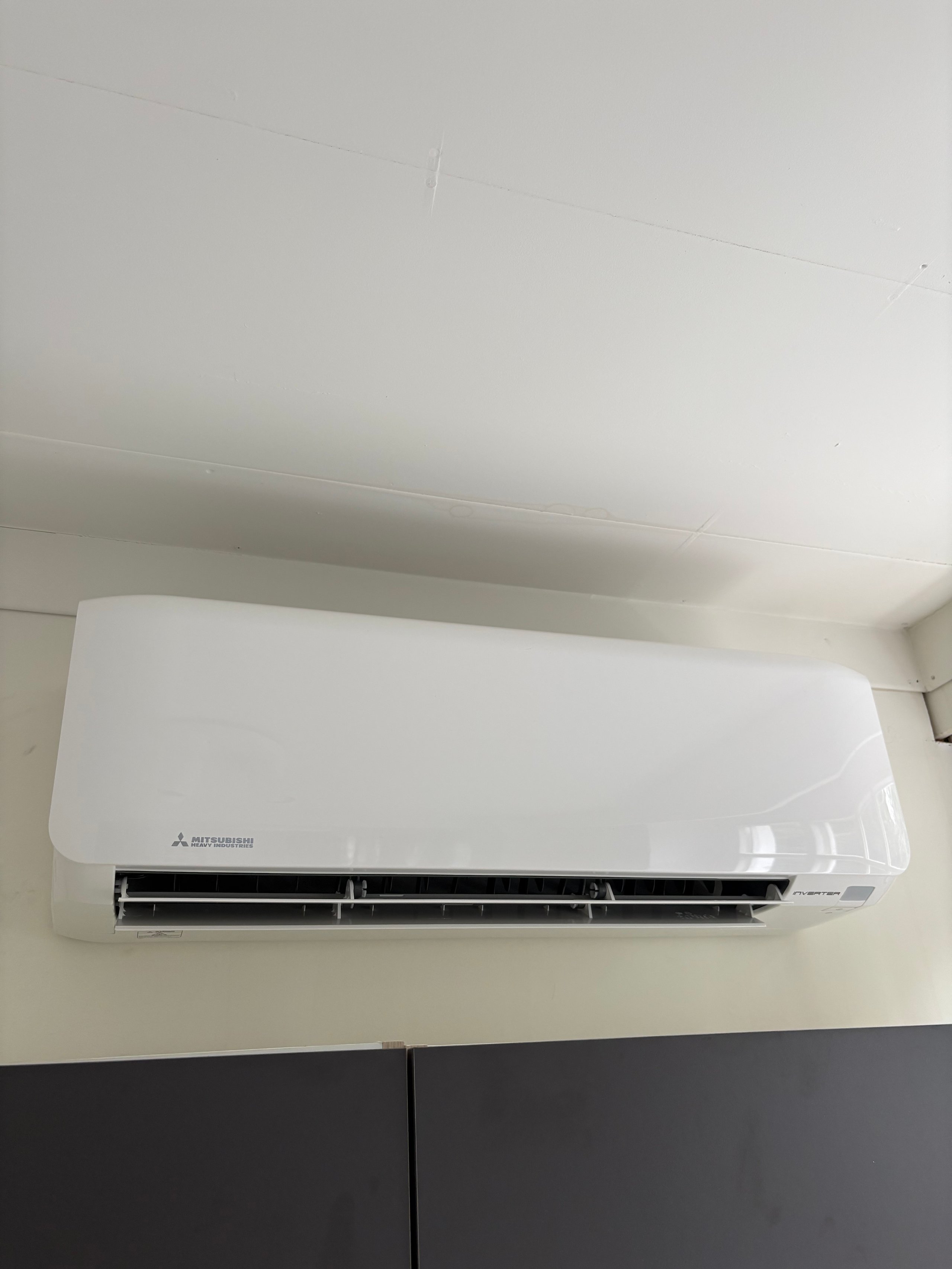 White Mitsubishi split-type air conditioning unit mounted on a beige wall above black trim