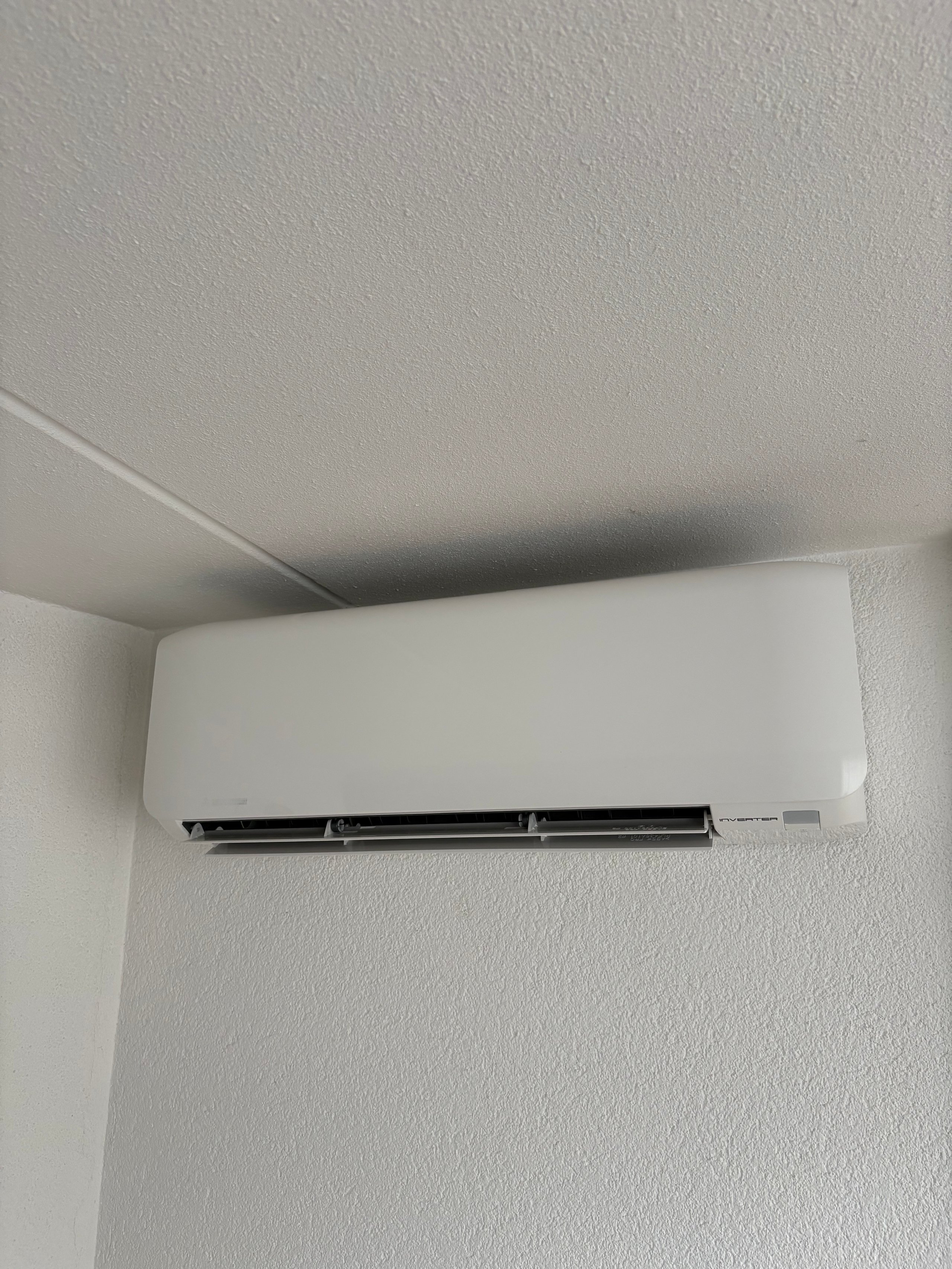 White split-type air conditioning unit mounted on a wall near the ceiling