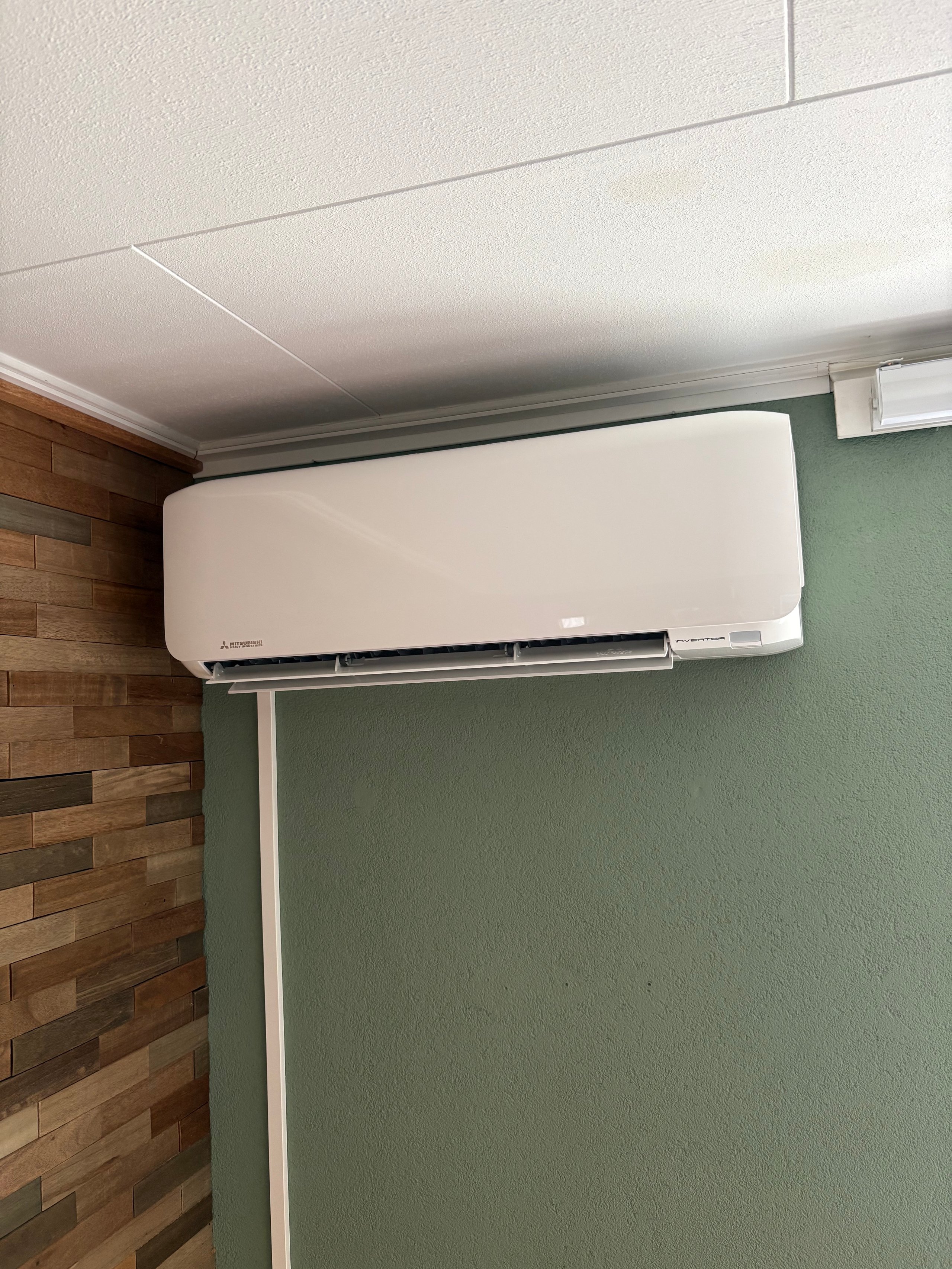 White wall-mounted air conditioning unit on green-painted wall with wooden accent paneling