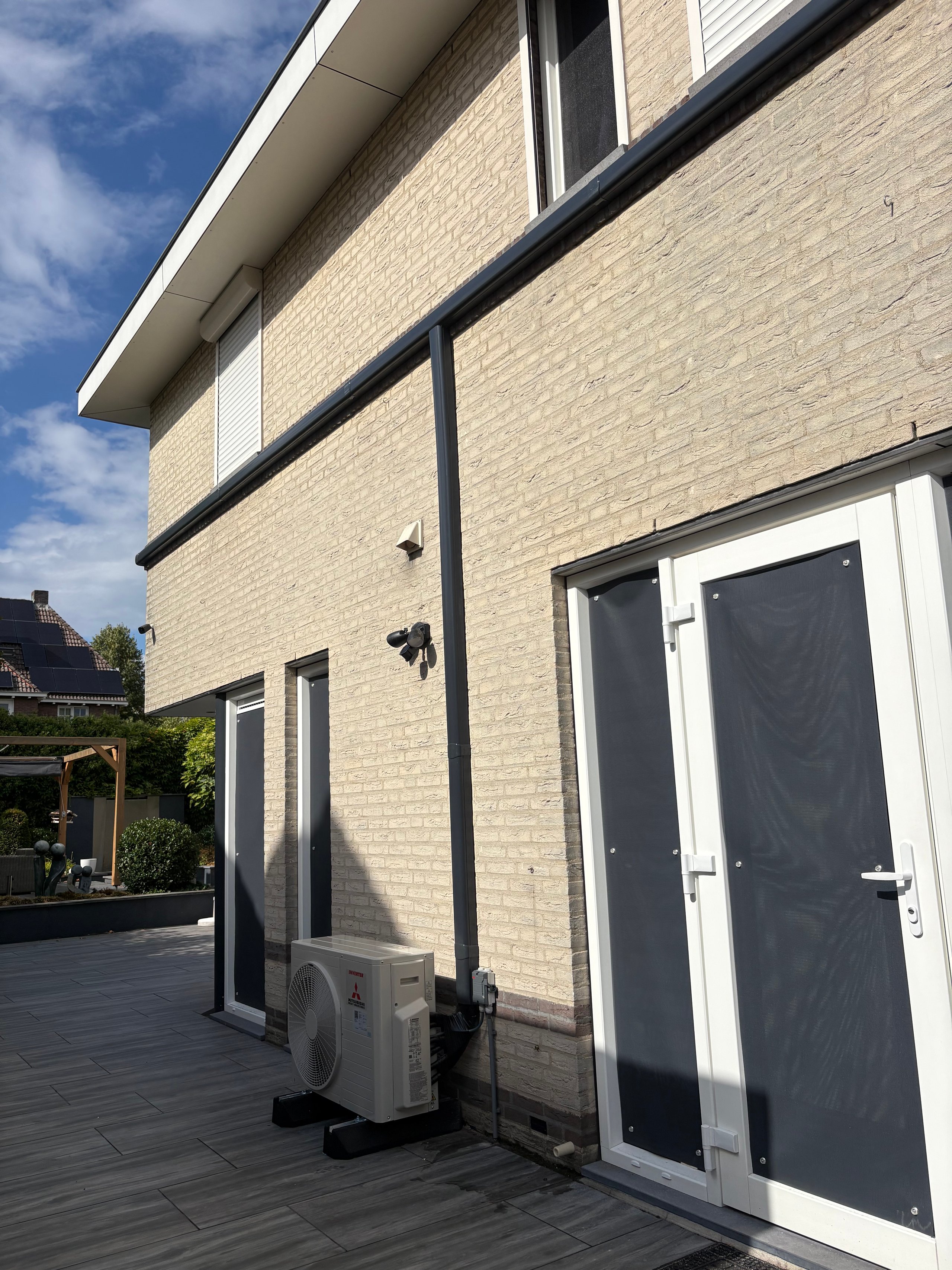 Modern brick house exterior with patio, white-framed glass doors, and outdoor air conditioning unit under blue sky