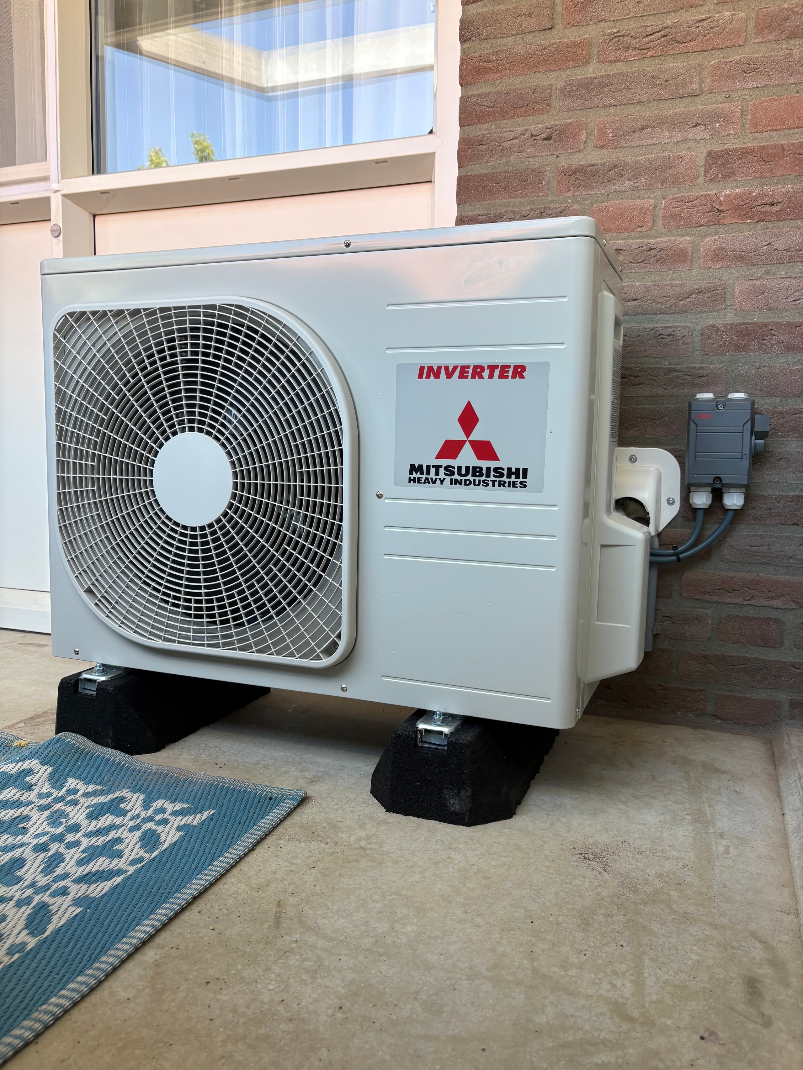 Mitsubishi inverter heat pump unit installed on exterior brick wall next to window