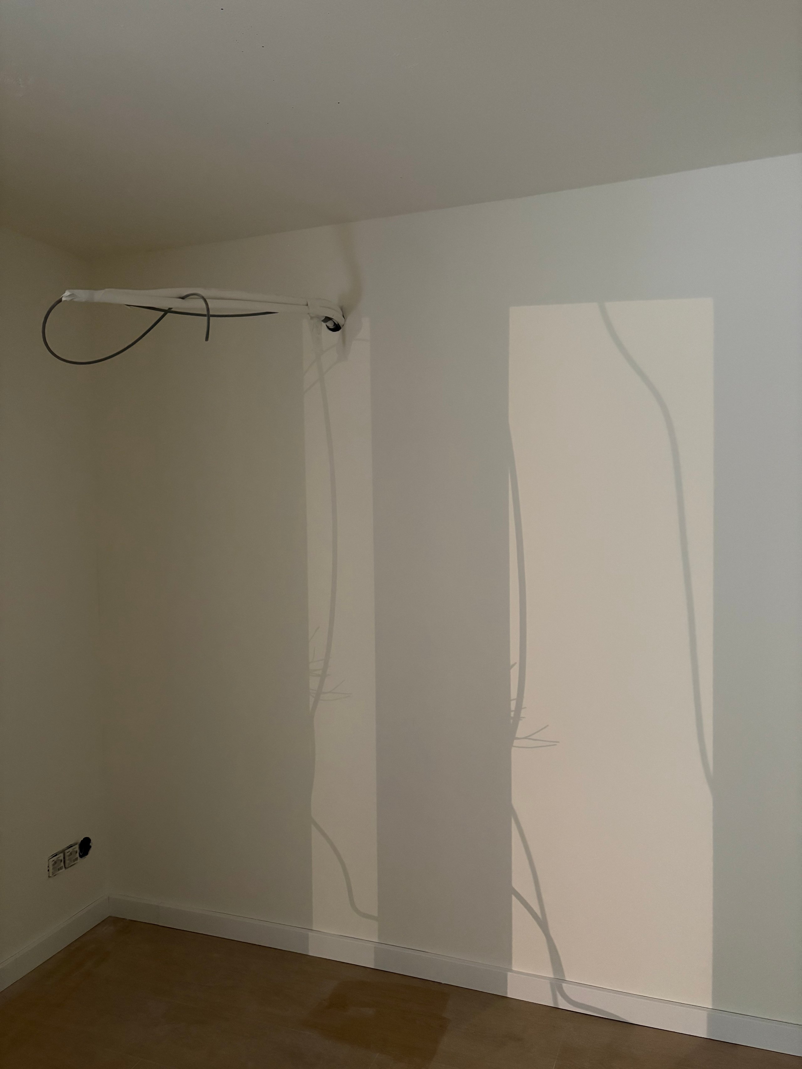 Empty room with white walls, electrical conduit running vertically, and a ceiling-mounted fixture with wiring