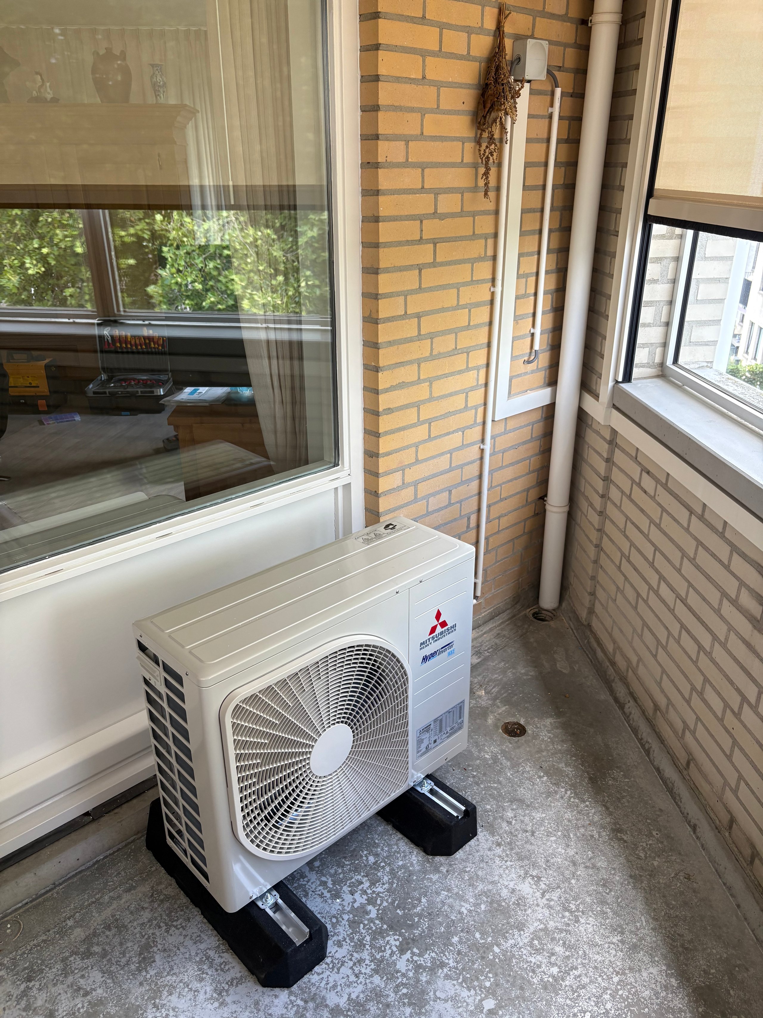 Mitsubishi air conditioning outdoor unit on concrete balcony between brick and windows