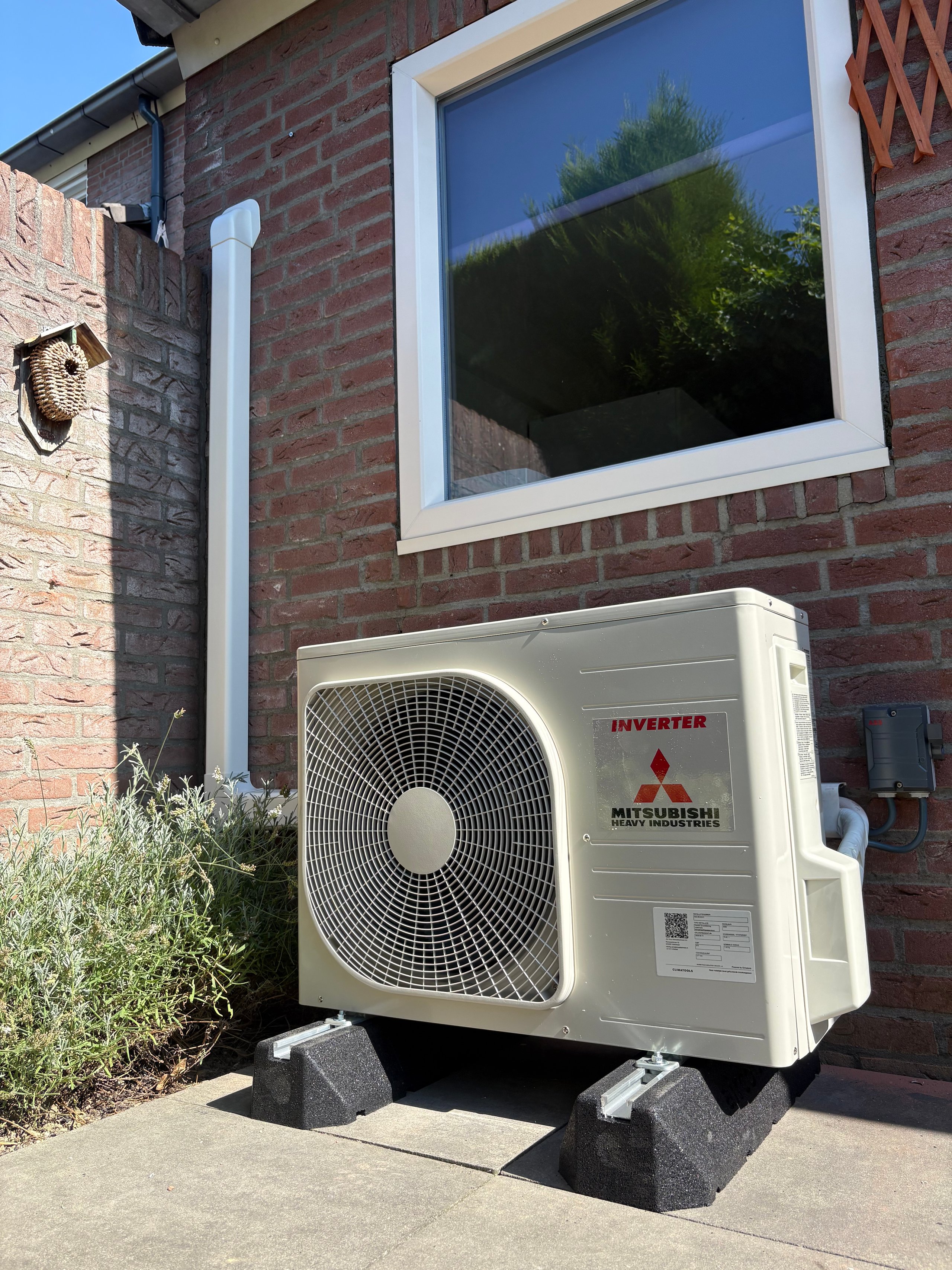 Mitsubishi inverter air conditioning outdoor unit mounted on a brick wall with reflection visible in window above