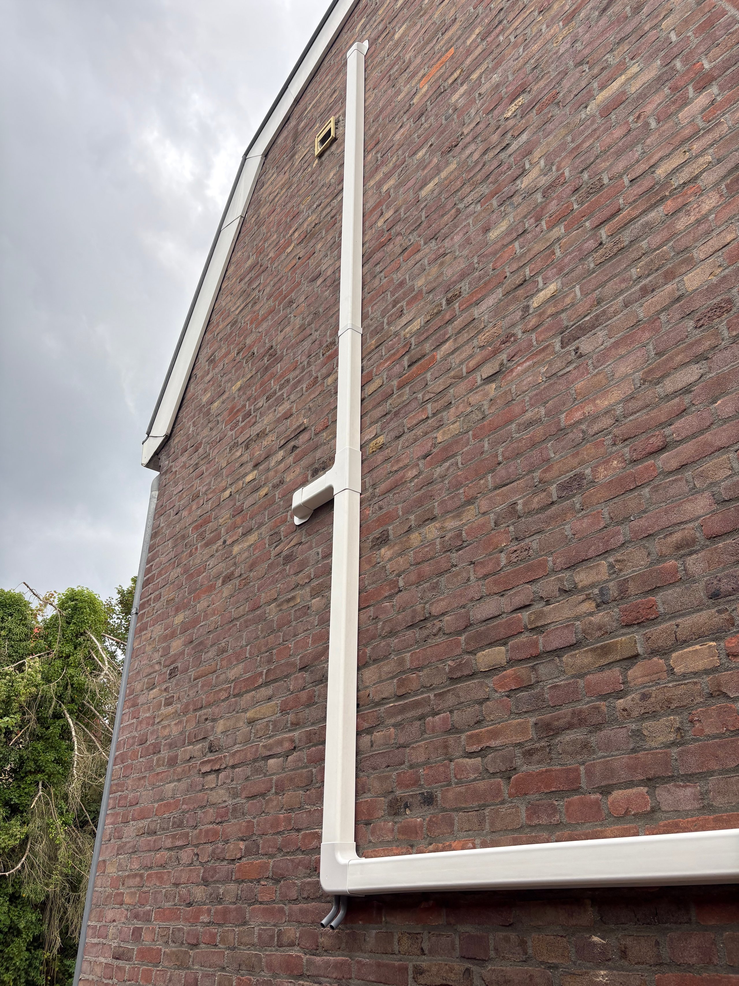 White downspout and gutter system on a brick building exterior against a cloudy sky