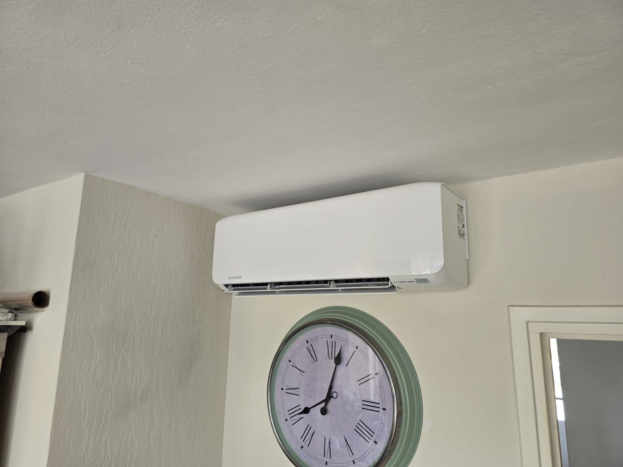 White split-type air conditioning unit mounted on wall above a green-framed analog clock in an interior room