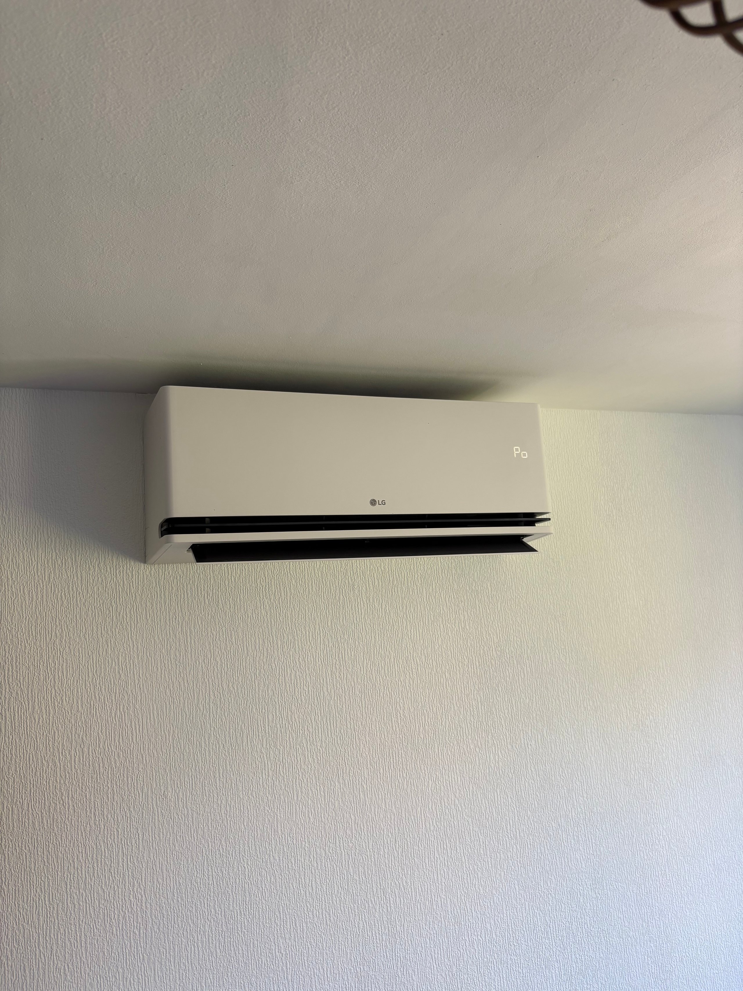 White wall-mounted air conditioning unit with black horizontal vent, installed on a light textured wall
