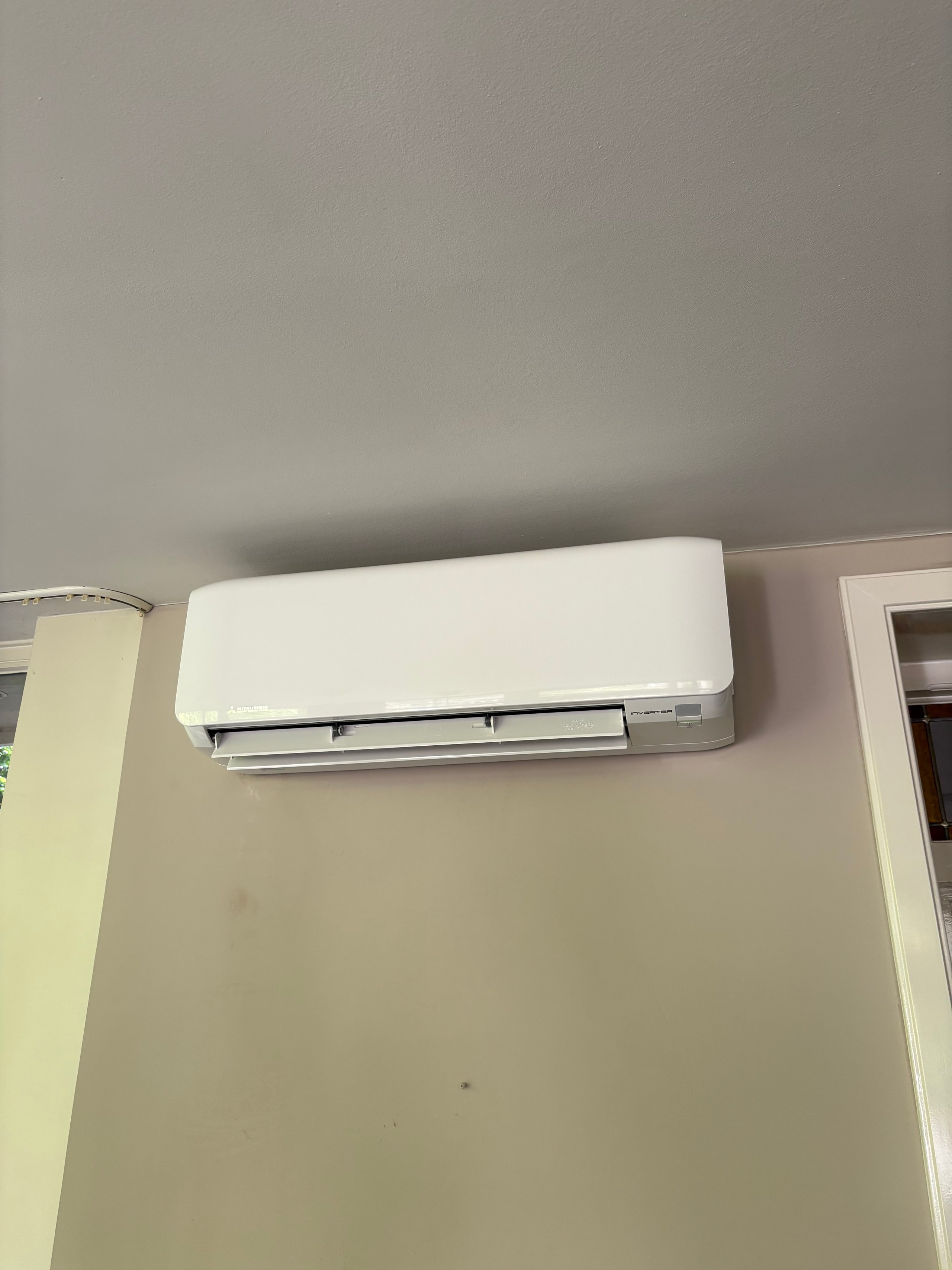 White wall-mounted ductless air conditioning unit installed on a beige wall with trim visible on the right side