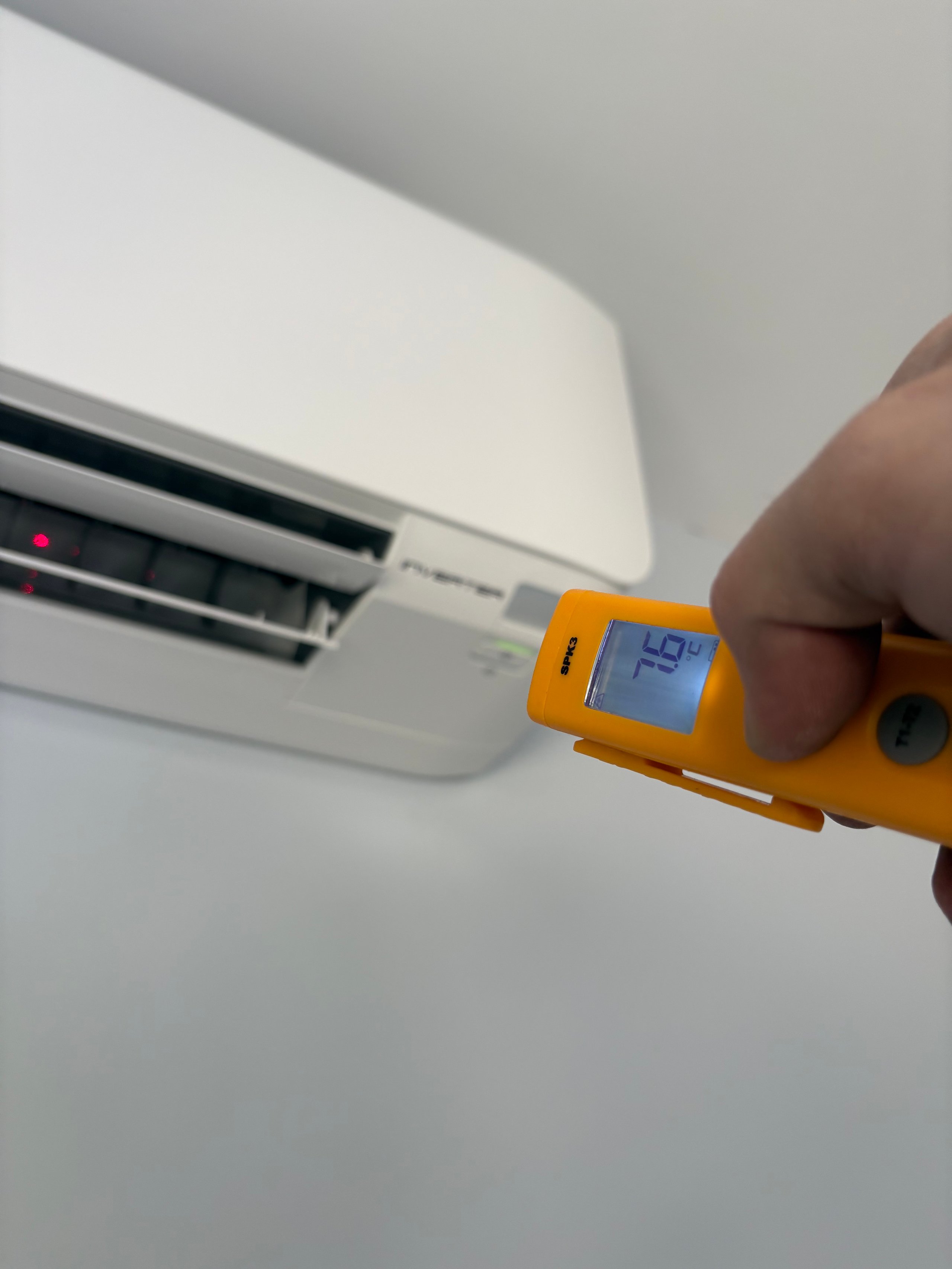 Hand holding a yellow temperature gun checking air conditioning unit