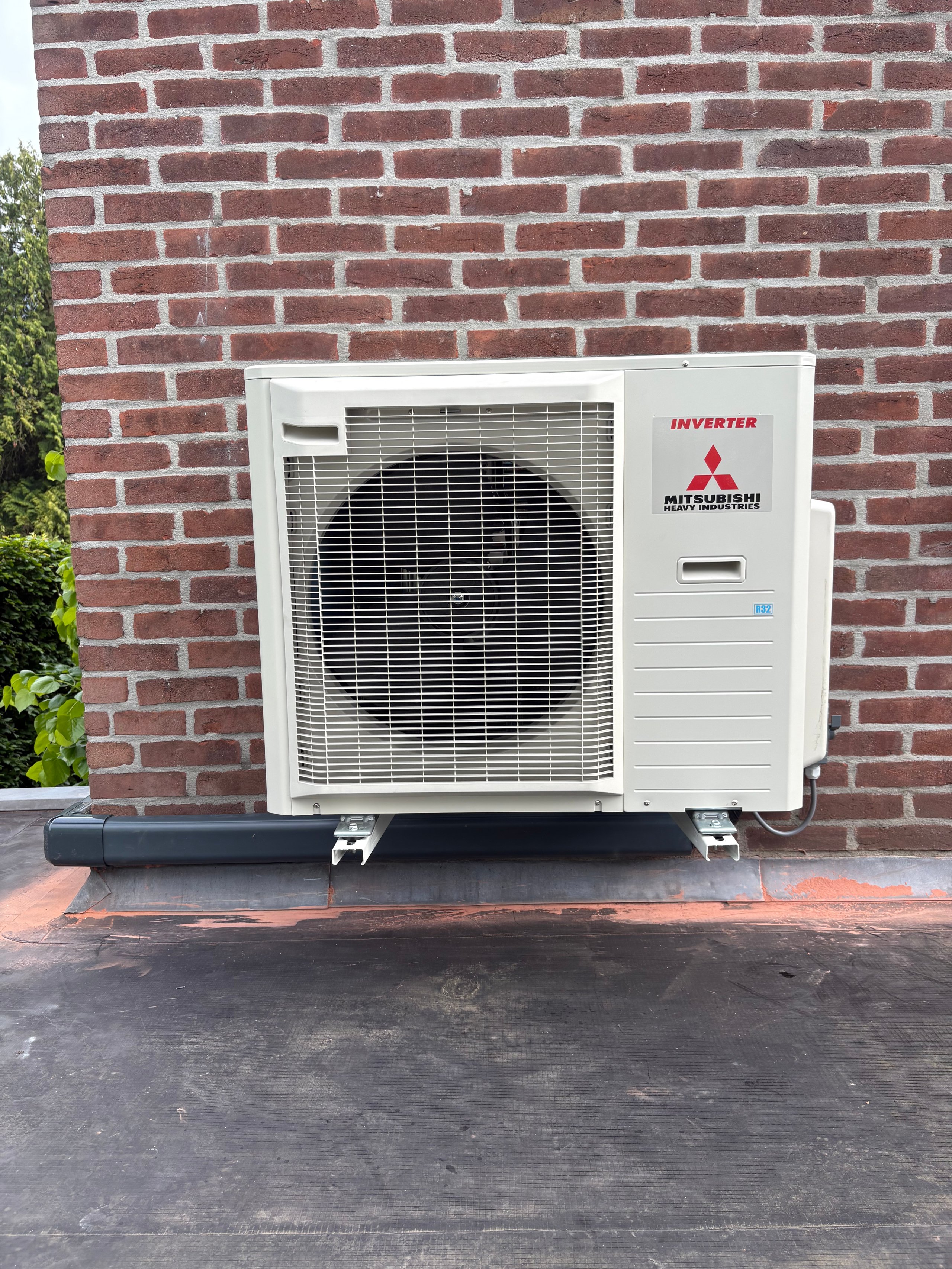 White Mitsubishi inverter air conditioning unit mounted on brick wall above asphalt base