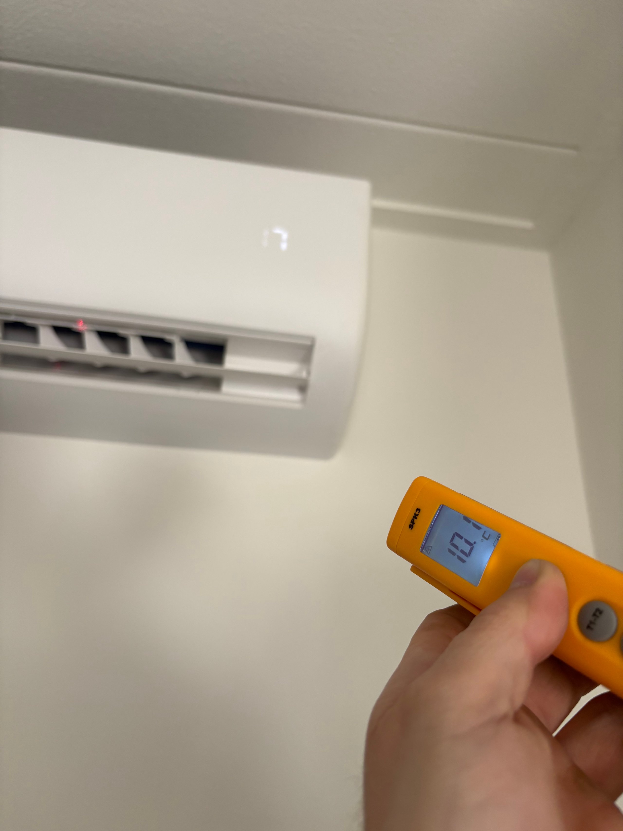 Hand holding digital level tool in front of white wall-mounted air conditioning unit