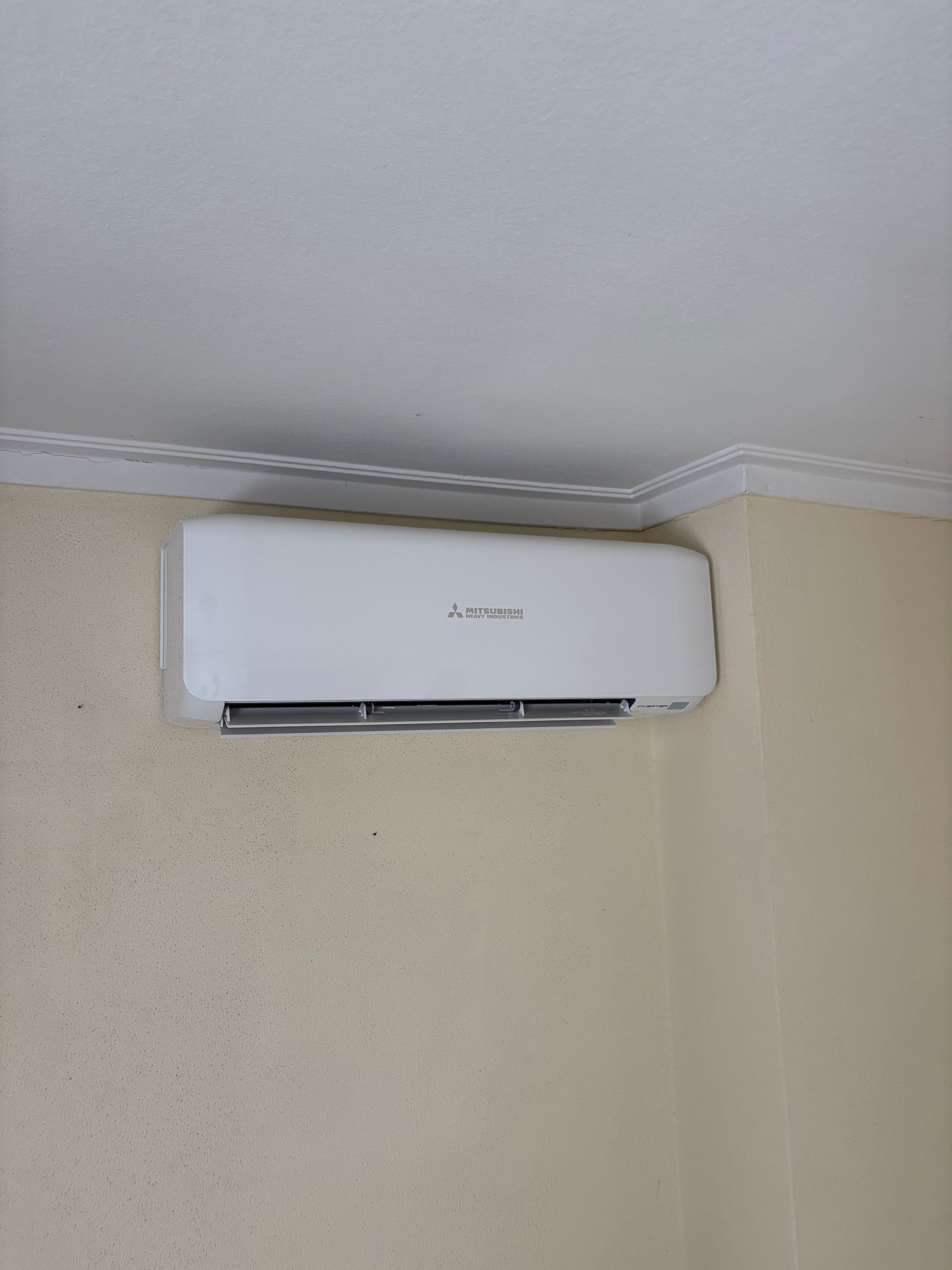 White Mitsubishi air conditioning unit mounted on a beige wall below a gray ceiling