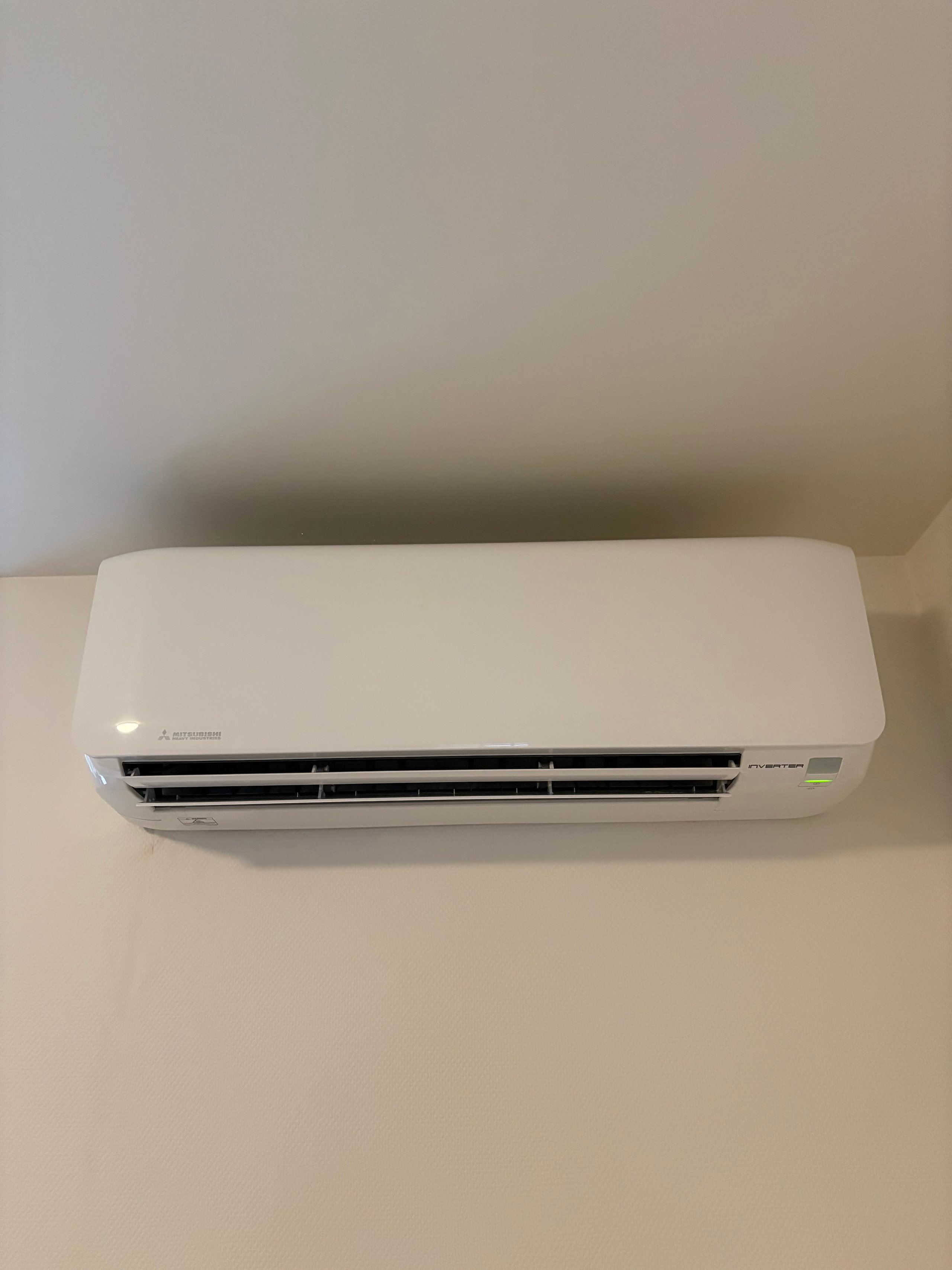 White wall-mounted air conditioning unit with black horizontal vents installed on a beige wall