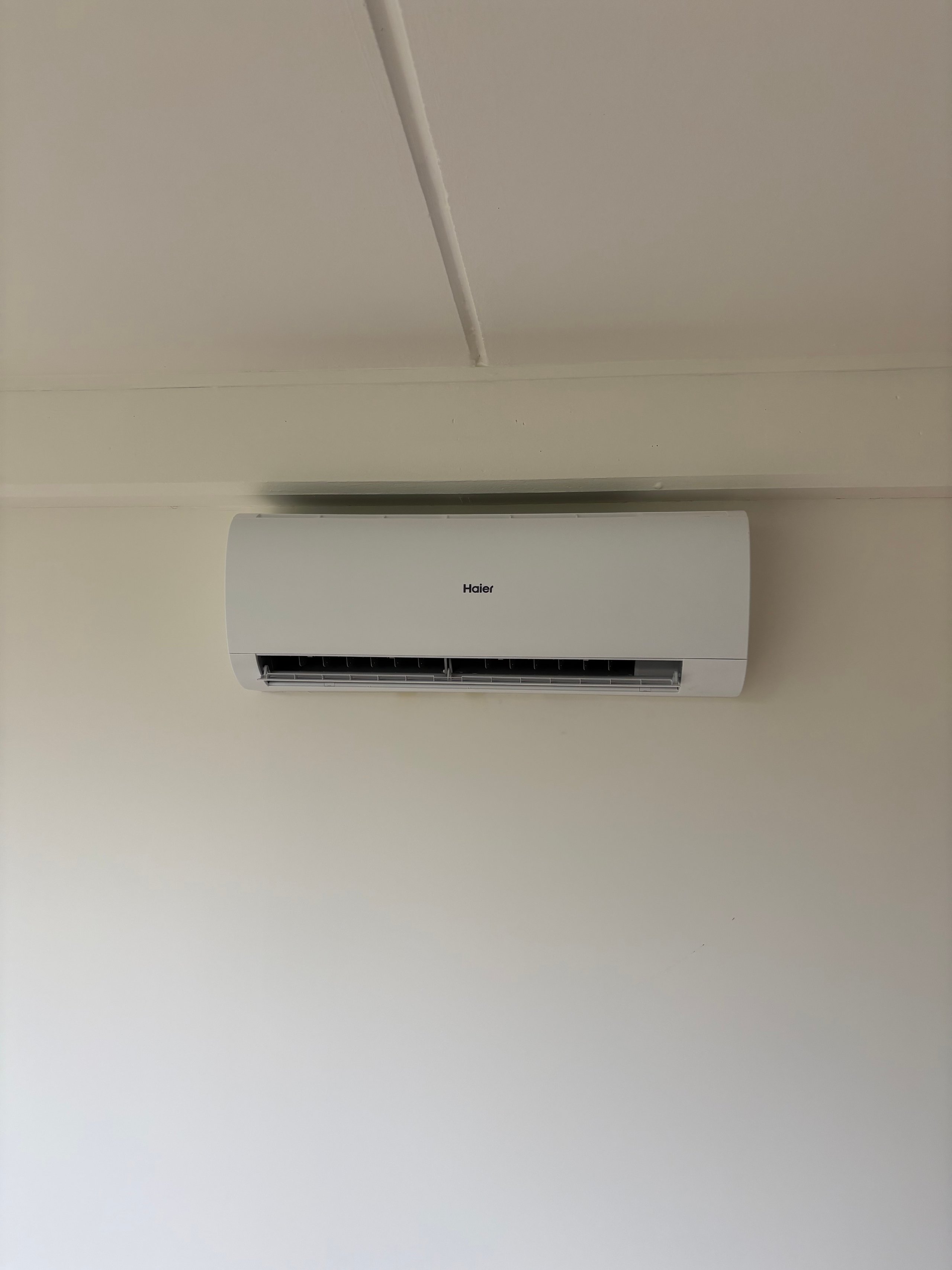 White Haier air conditioning unit mounted on a light wall with a gray pipe extending from above
