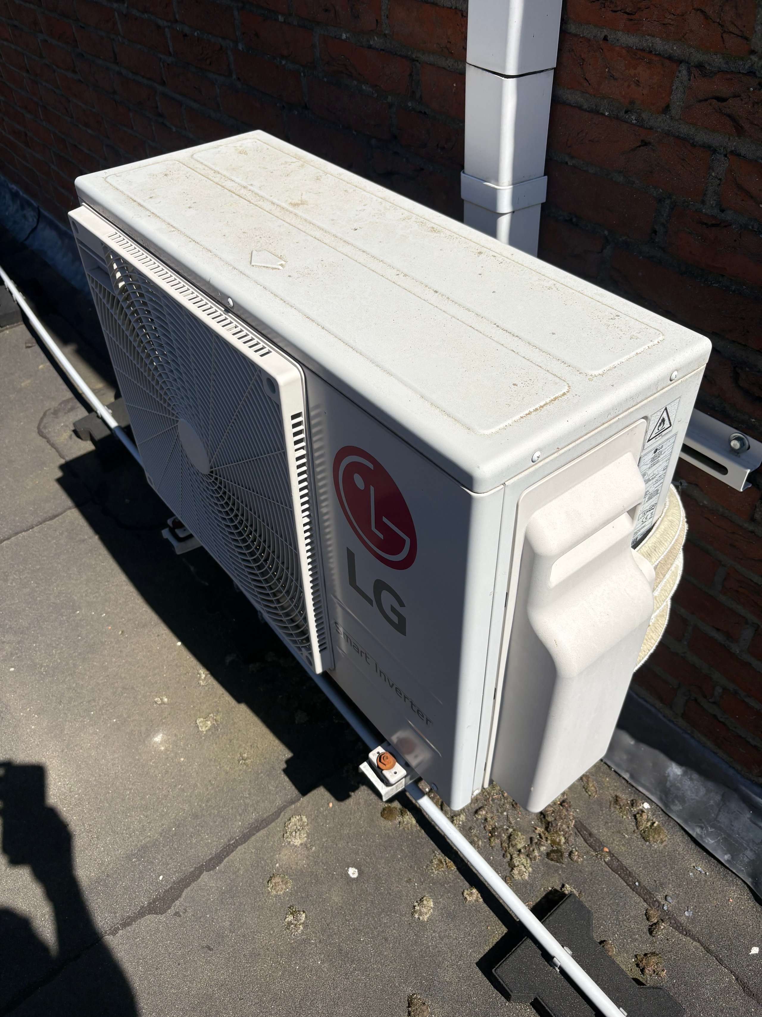 LG air conditioning outdoor unit mounted on a brick wall with copper refrigerant lines and white metal tubing visible