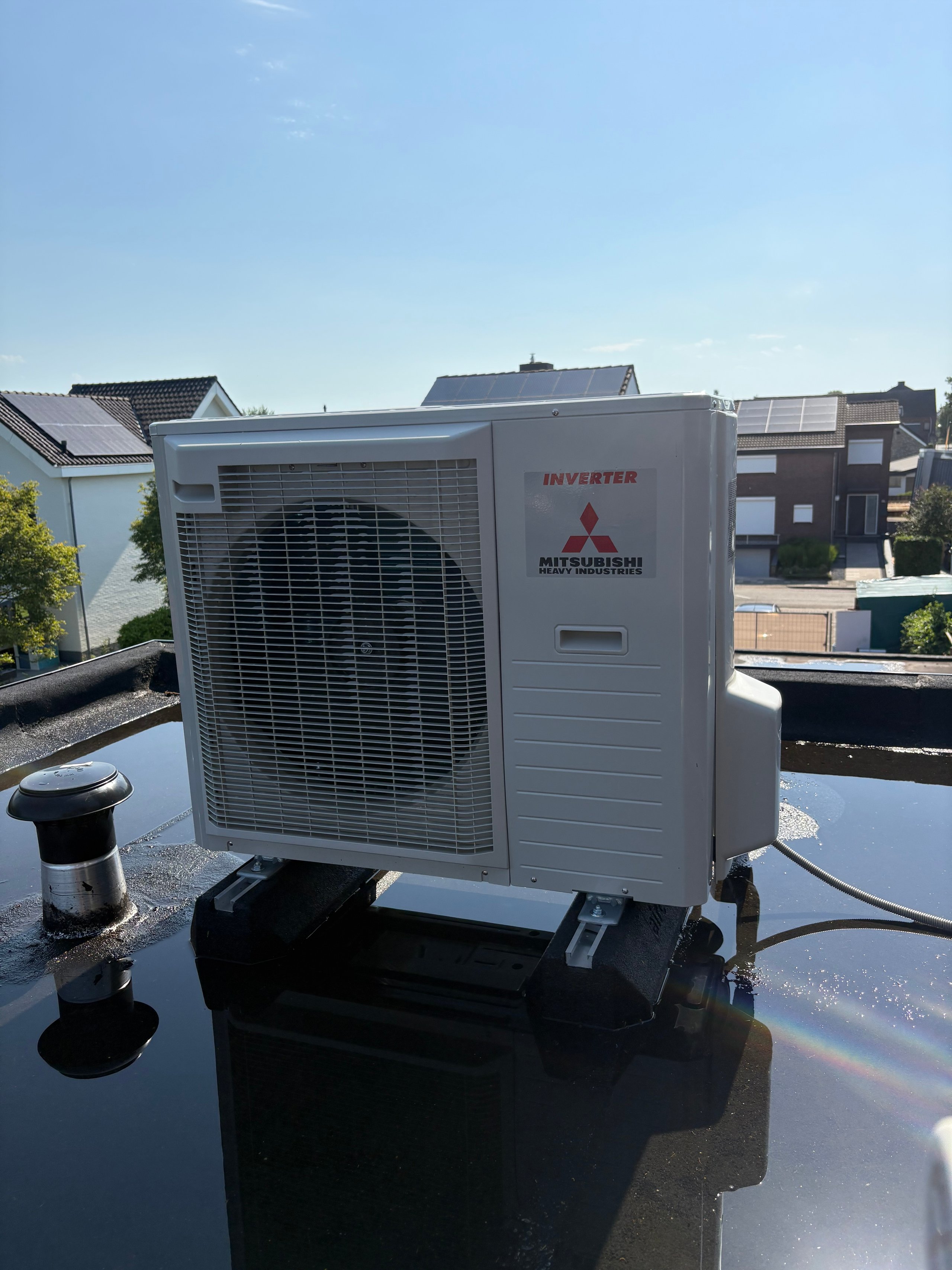 Mitsubishi inverter air conditioning unit mounted on a residential rooftop with suburban houses in background