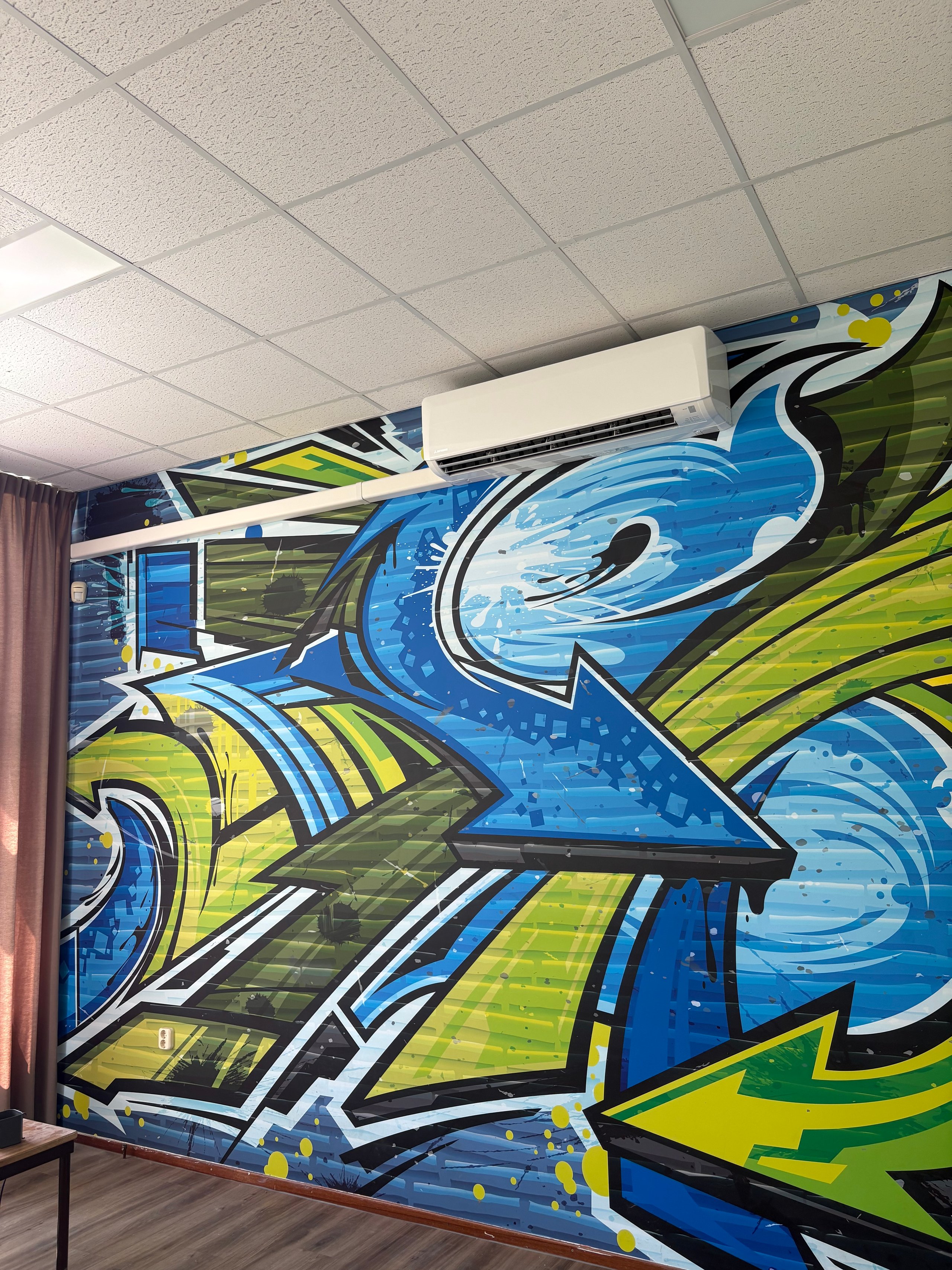 Colorful blue and lime green graffiti mural with bold strokes and lettering on an interior wall