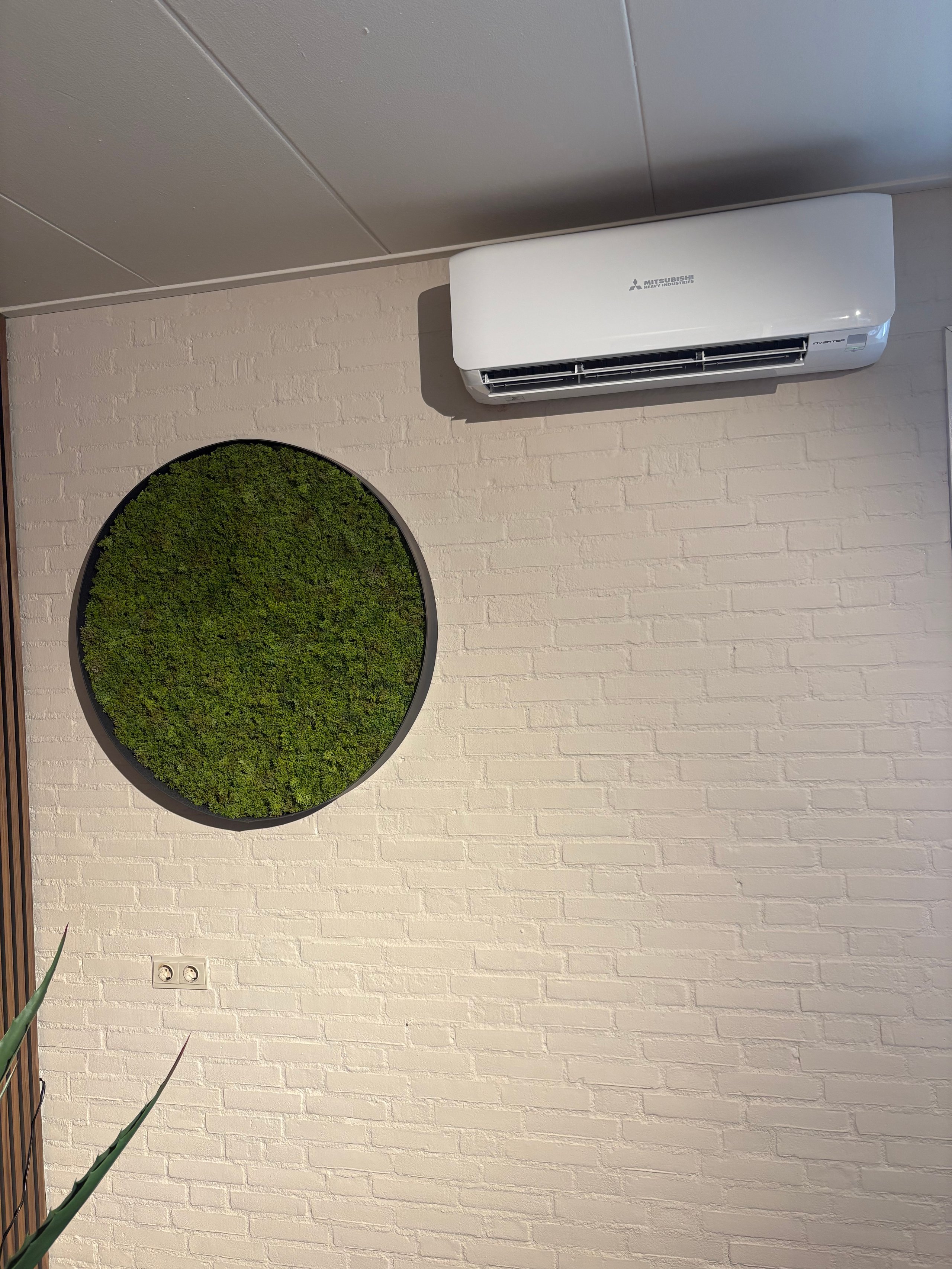 White brick wall with round moss artwork and air conditioning unit mounted above