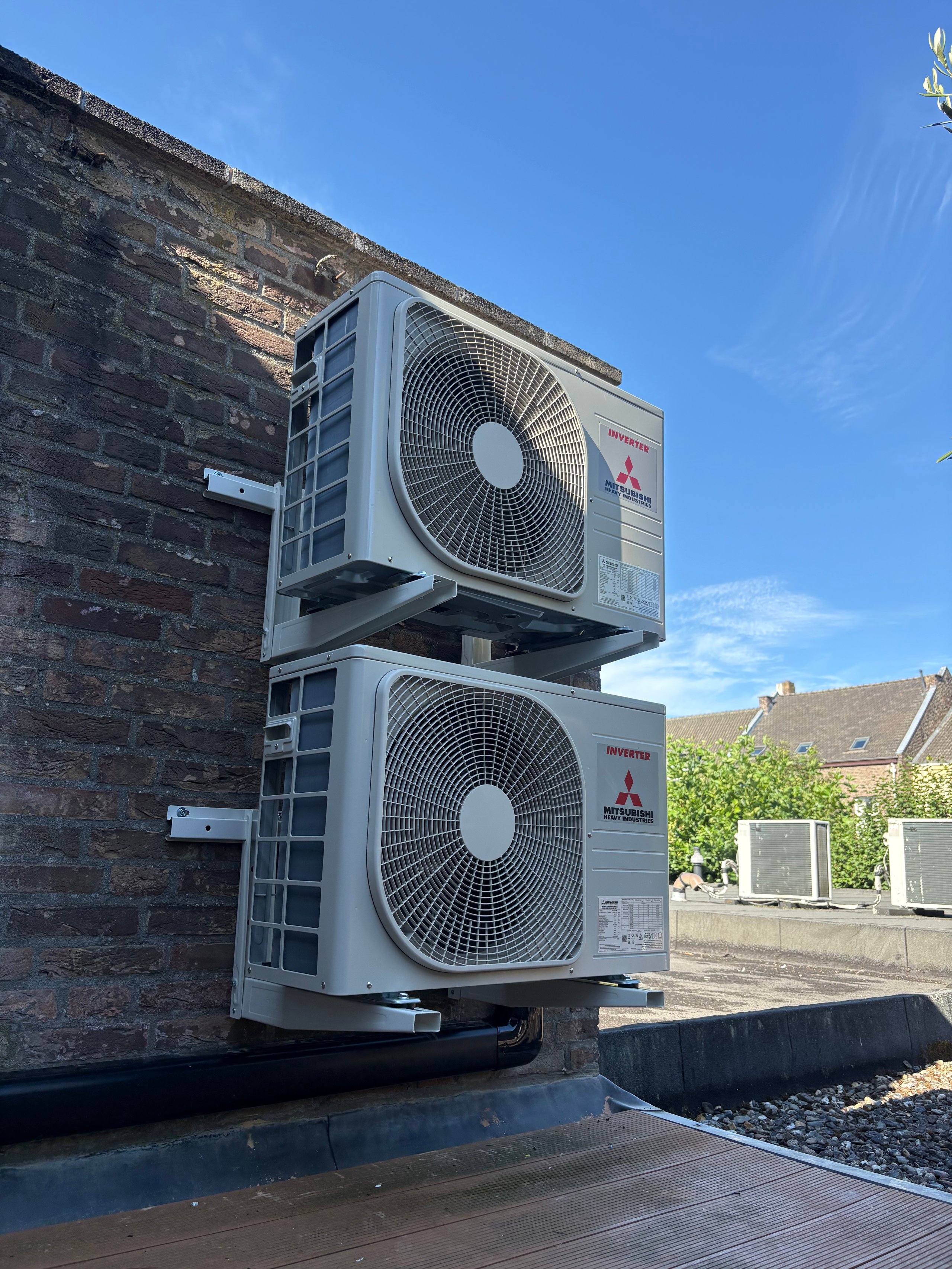 Two stacked Mitsubishi air conditioning units mounted on a brick building wall against a clear blue sky