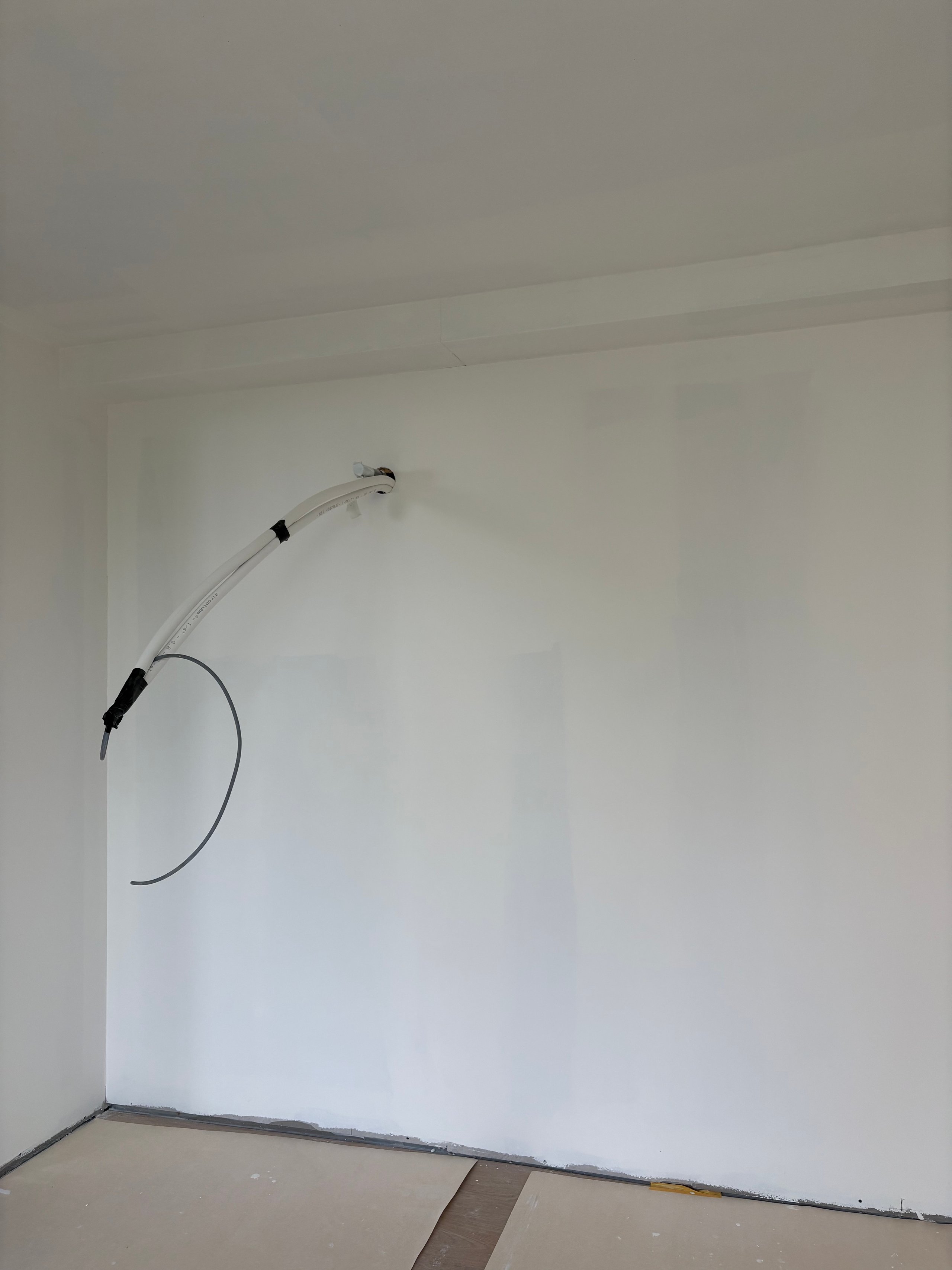 White wall with curved electrical wire or conduit looped from floor to mid-wall height