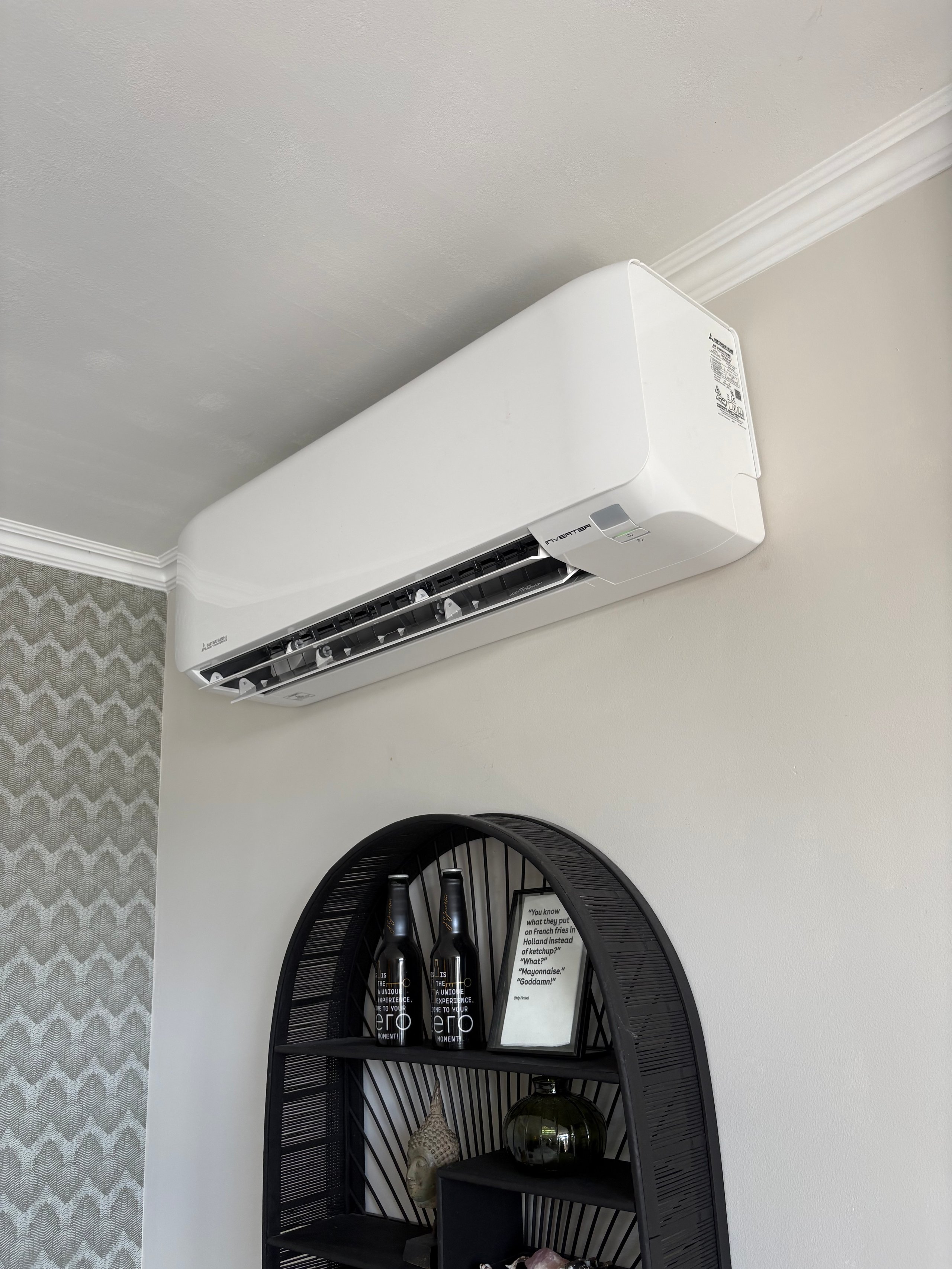 White wall-mounted ductless air conditioning unit above a black wicker papasan chair in a residential room