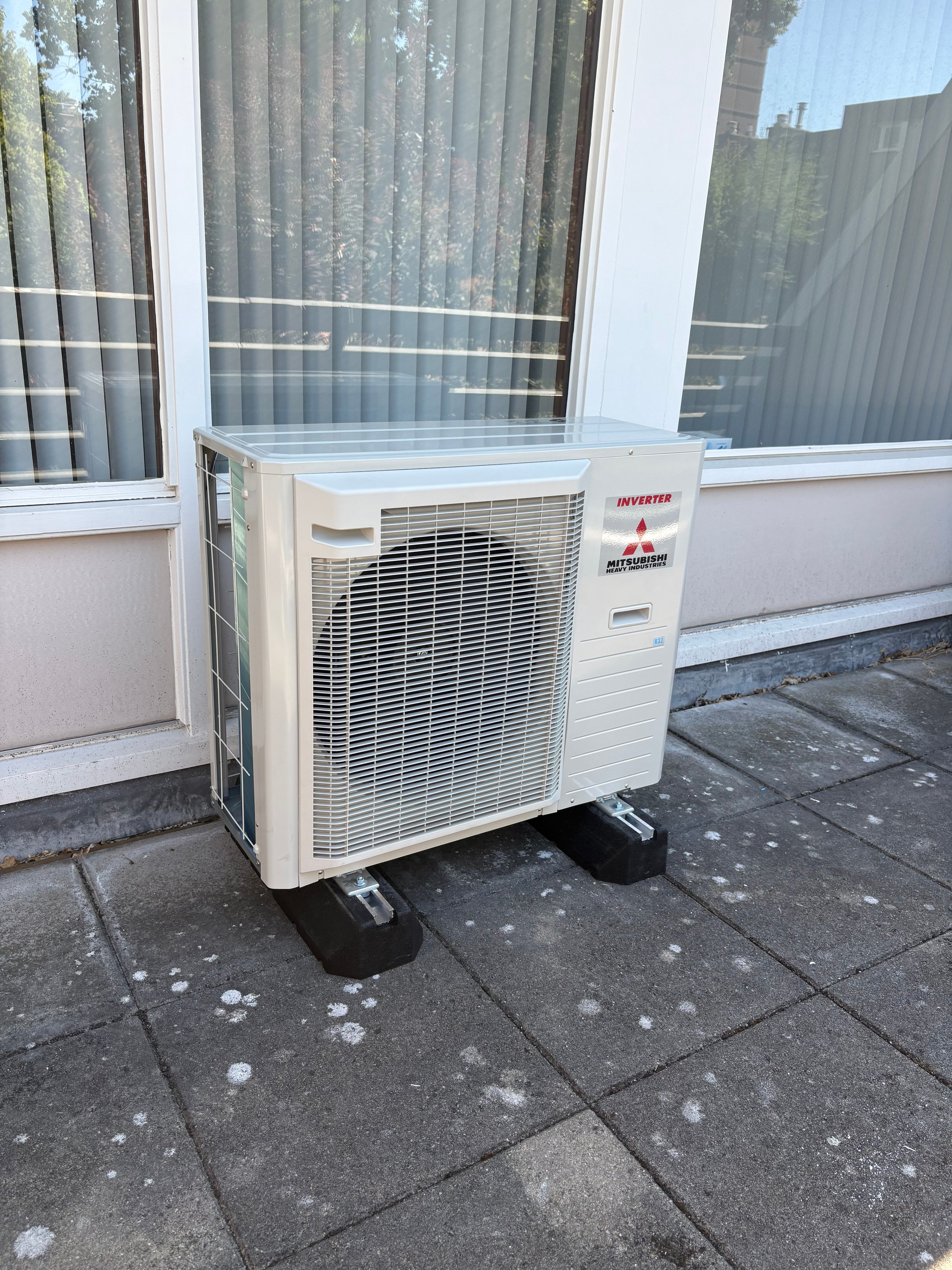 White outdoor air conditioning unit on concrete patio beside glass doors and windows