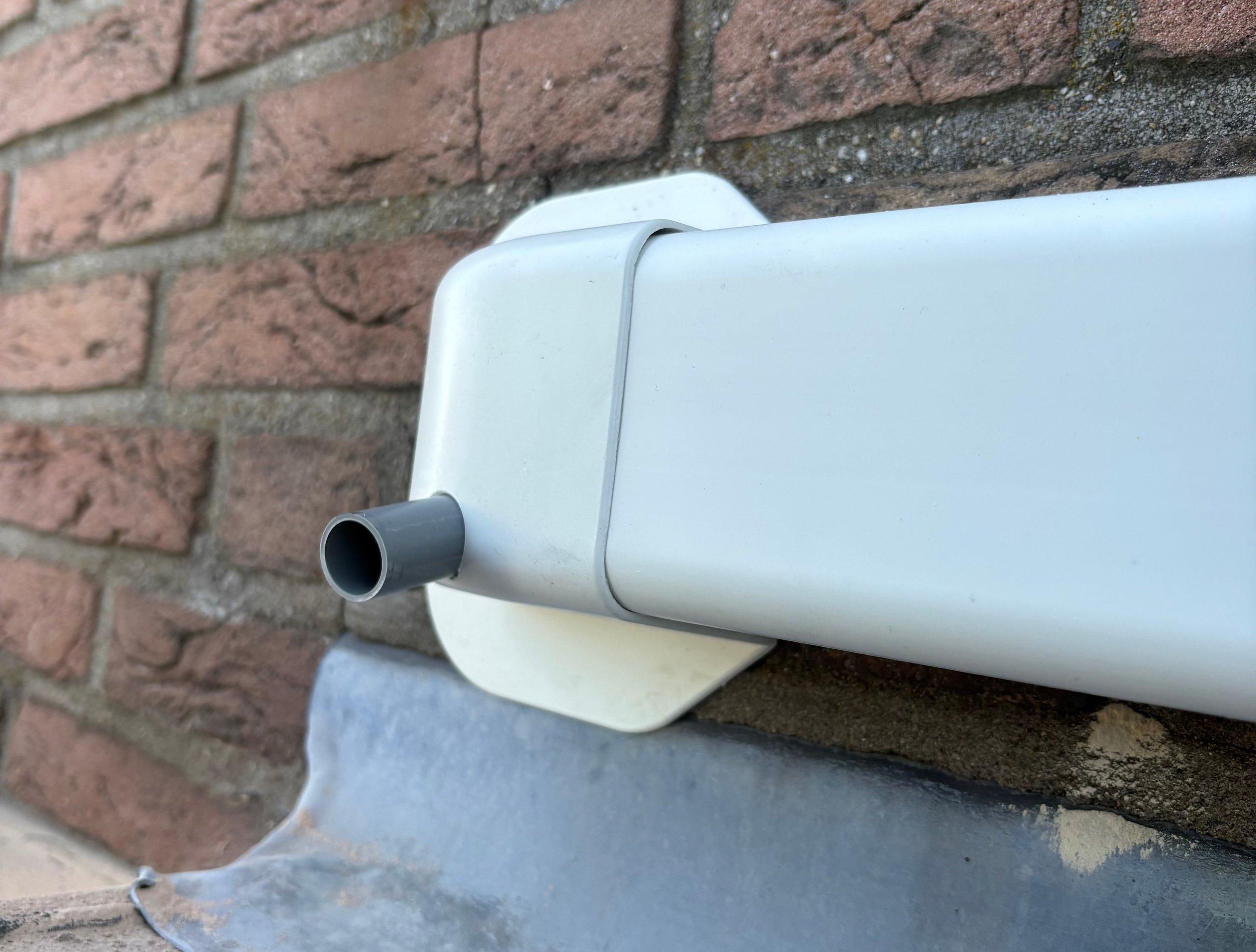 White downspout and gutter attached to red brick wall