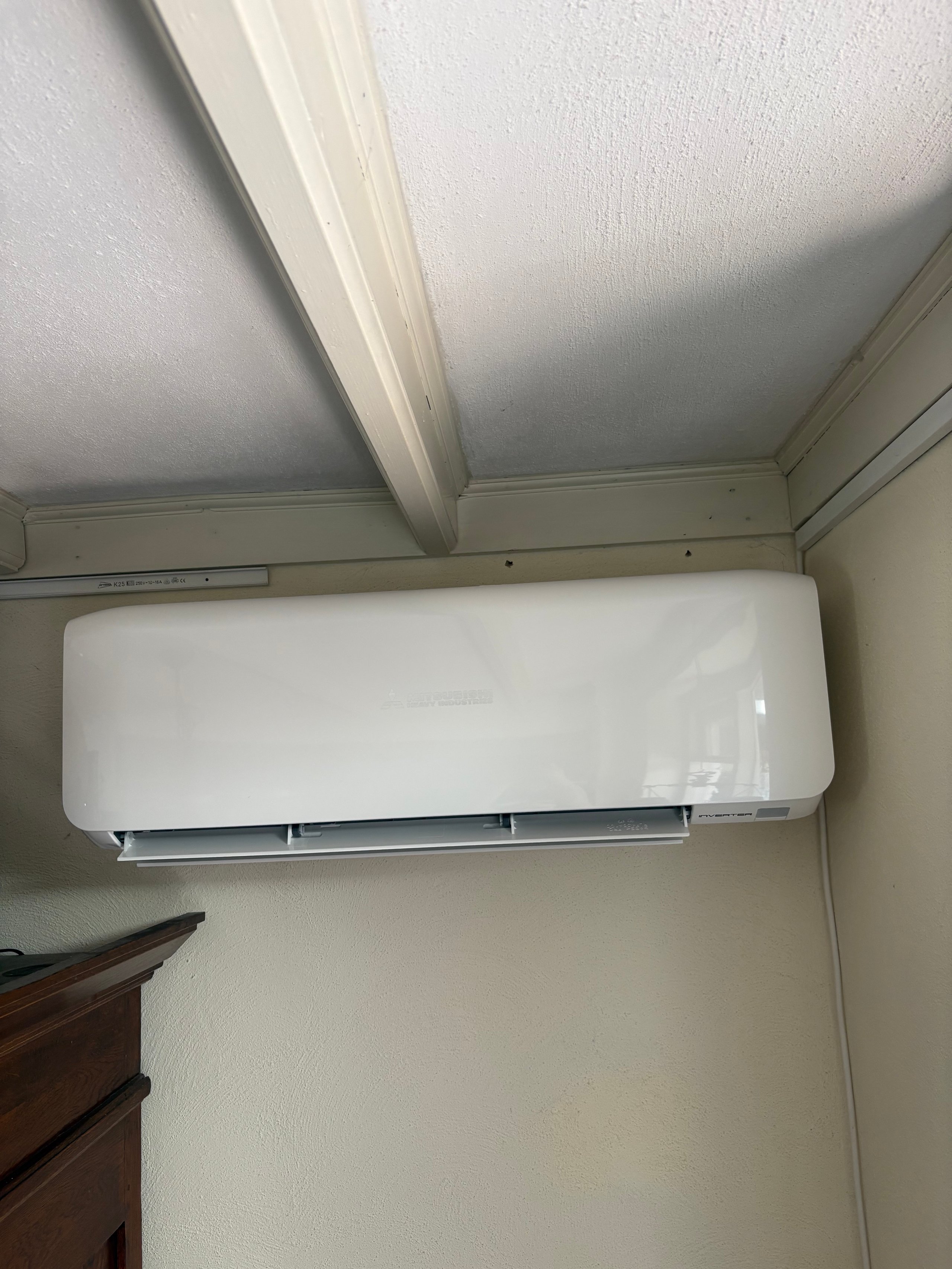 White wall-mounted ductless air conditioning unit installed on beige wall beneath exposed ceiling beam