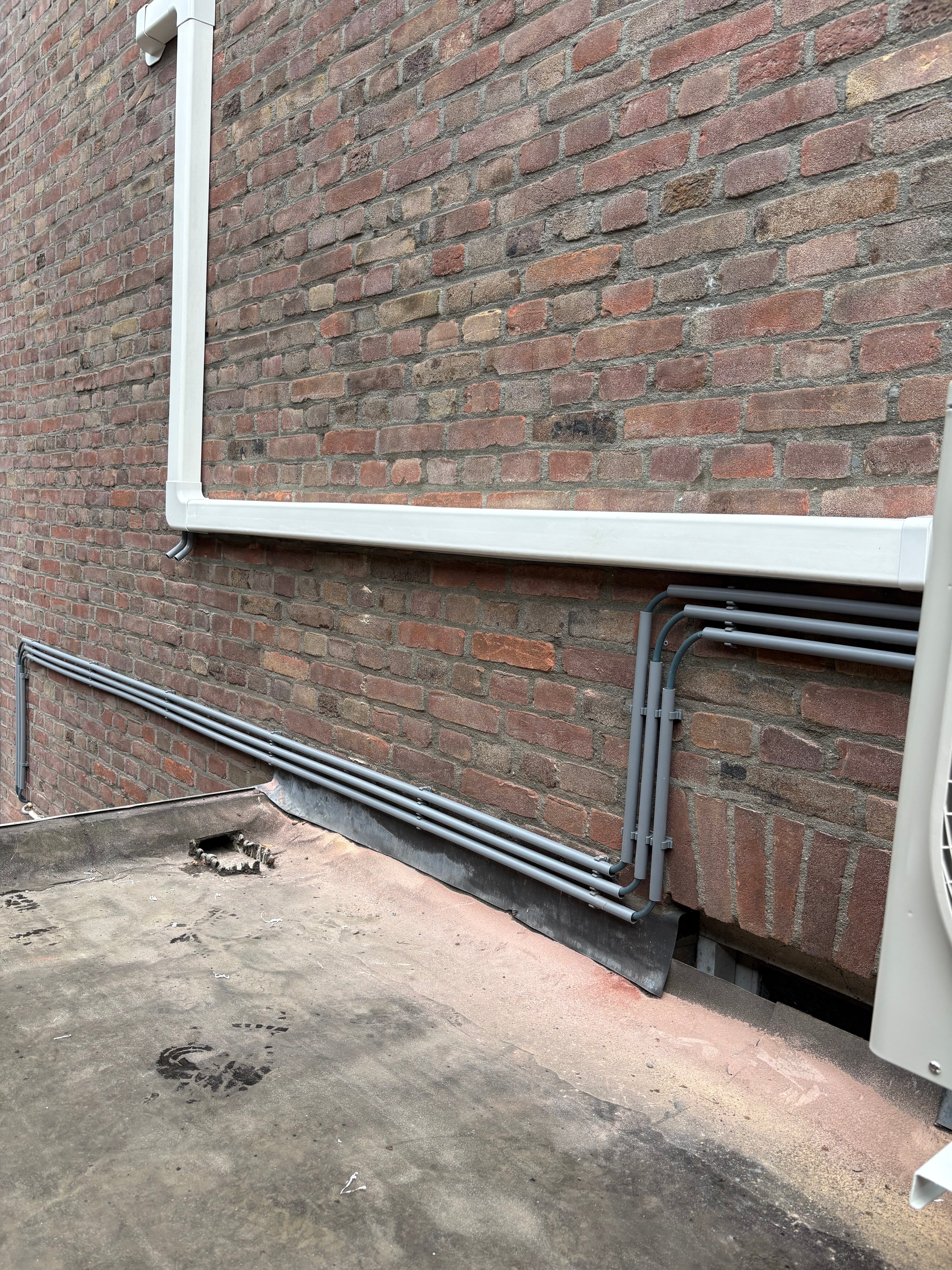 Red brick wall with white and black utility pipes and conduit attached to the surface