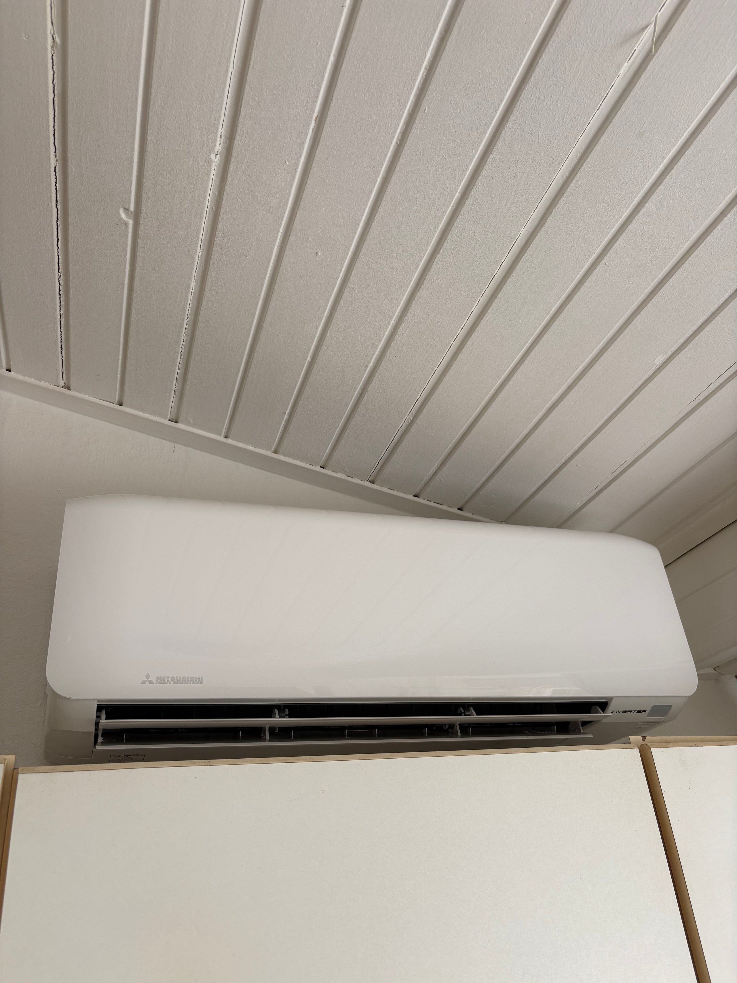 White wall-mounted air conditioning unit installed on a ceiling with diagonal metal beam details