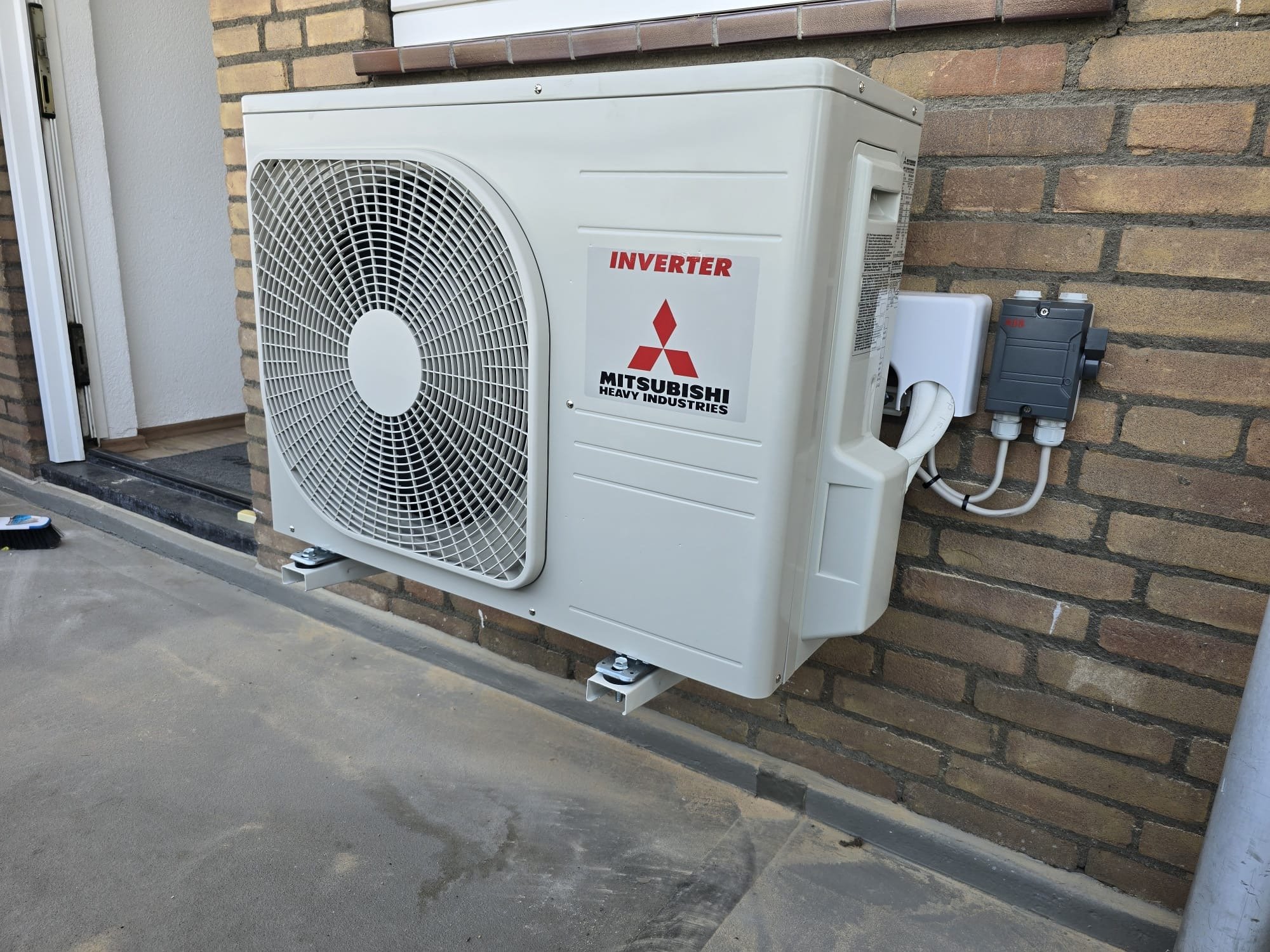 Mitsubishi inverter heat pump air conditioning unit mounted on exterior brick wall with outdoor condenser unit and control box