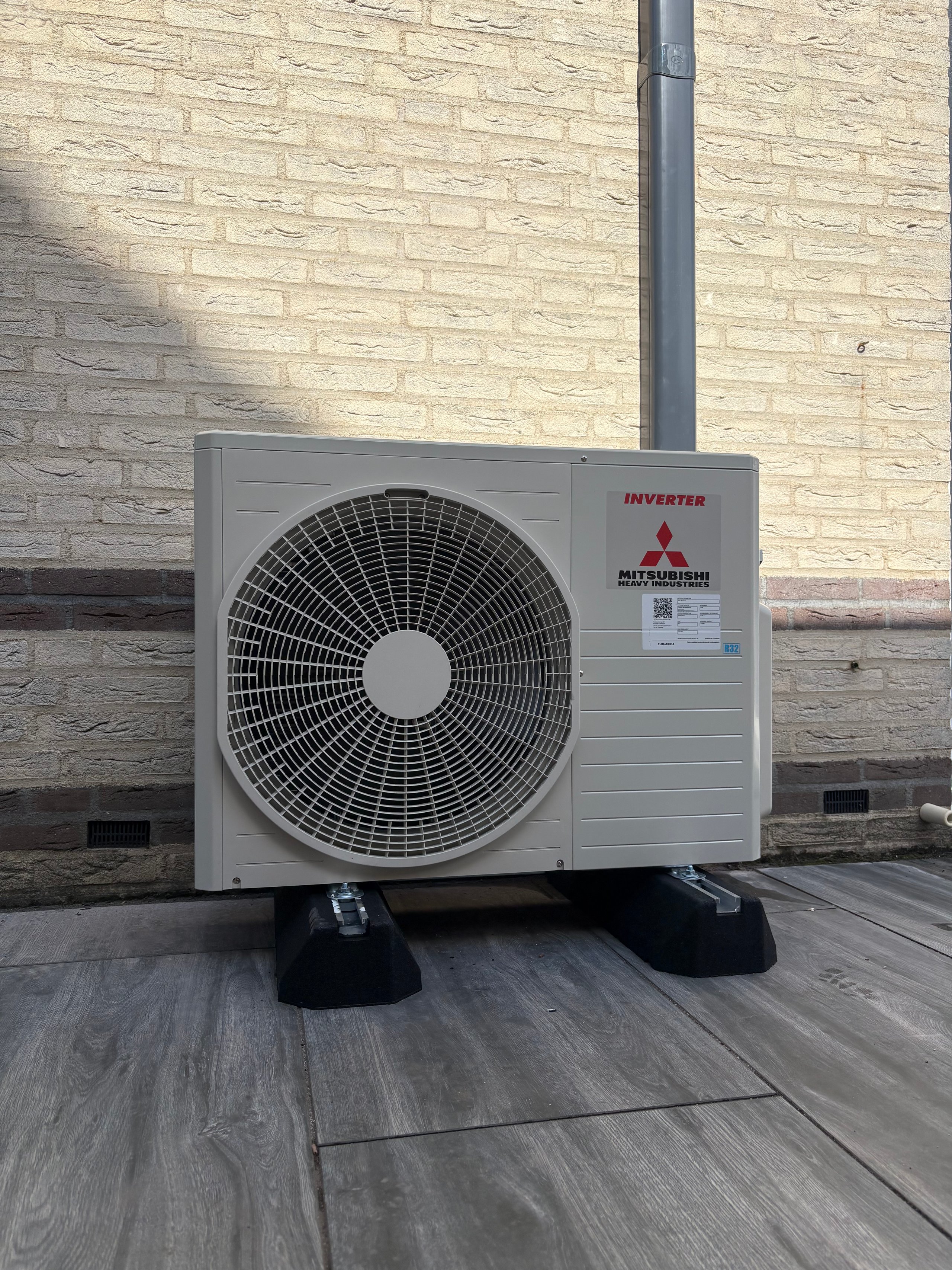 Mitsubishi inverter heat pump unit mounted on rubber pads against a brick building wall