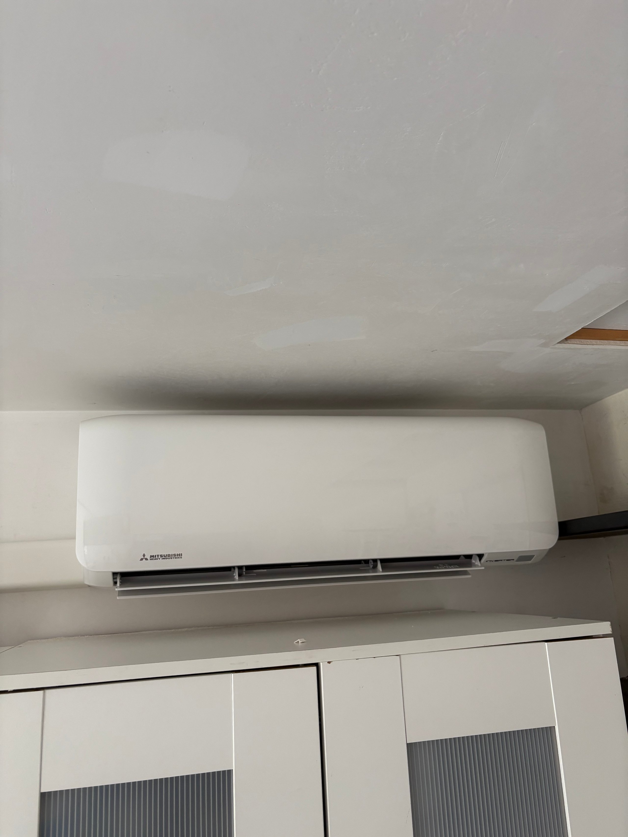 White Mitsubishi air conditioning unit mounted on wall above kitchen cabinets